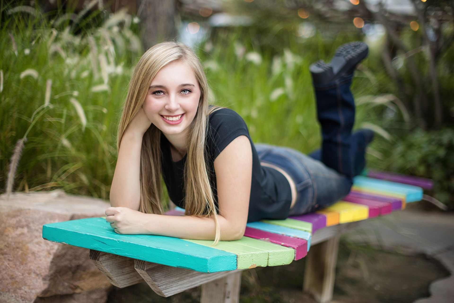 A young woman is laying on her stomach on a colorful bench.