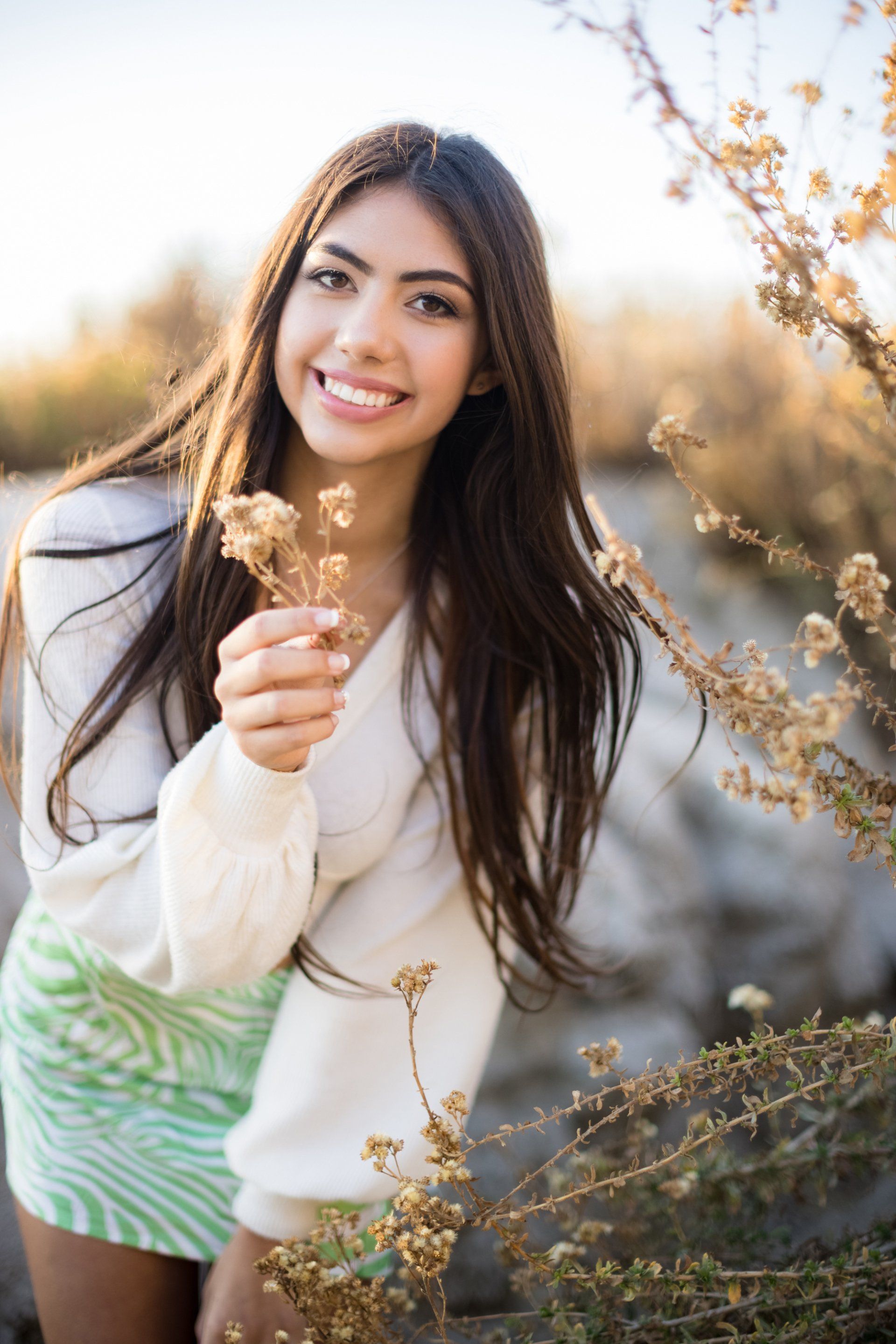 High school senior girl holding a flower at golden hour on the beach in Laguna Beach