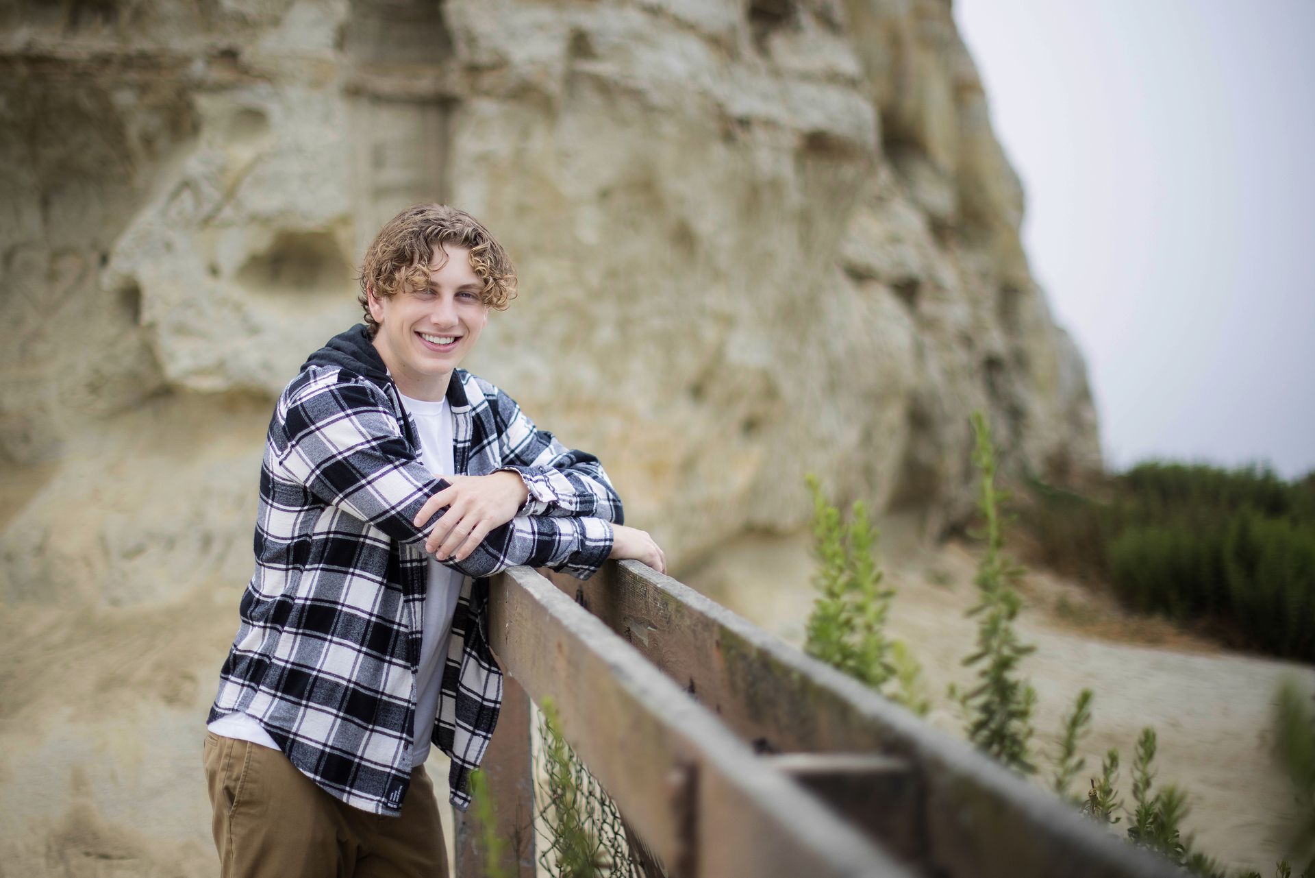 A young man in a plaid shirt is leaning on a wooden railing.
