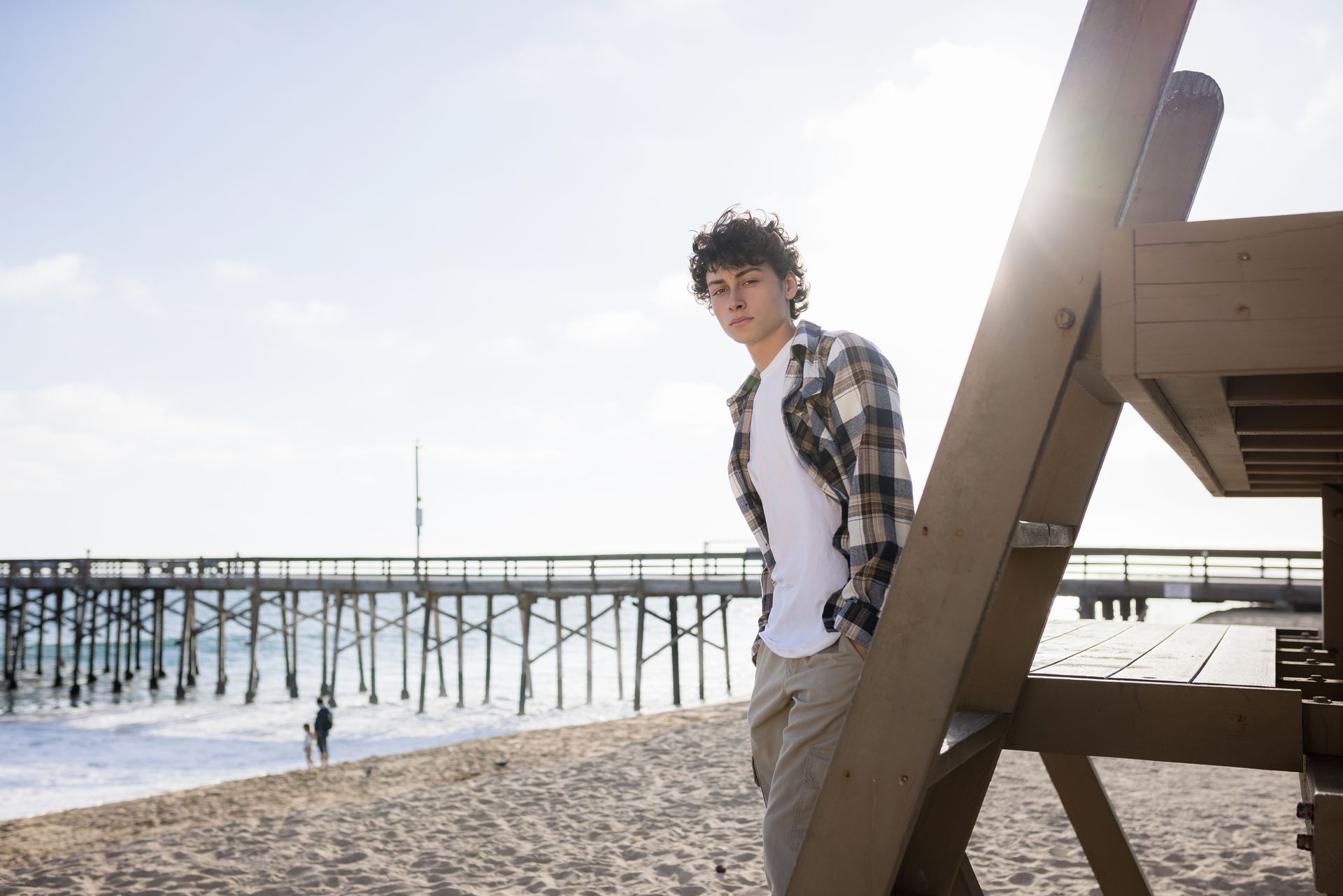 Person leaning on a wooden beach structure near the ocean at sunset