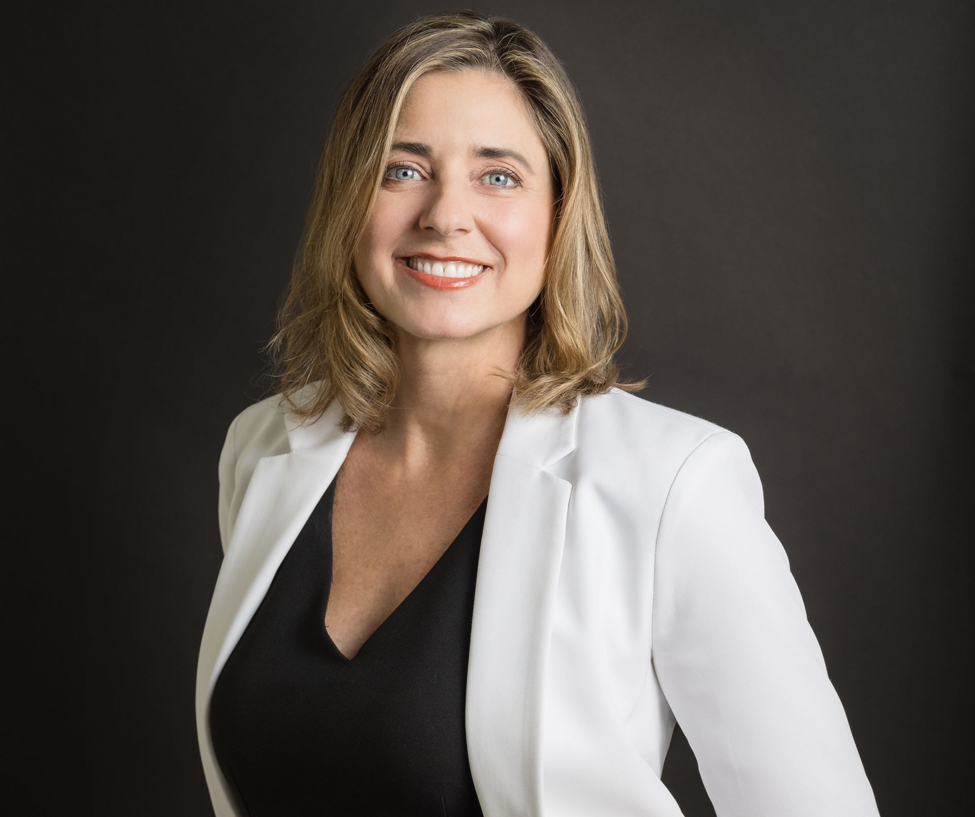 A woman wearing a white jacket and a black top smiles for the camera