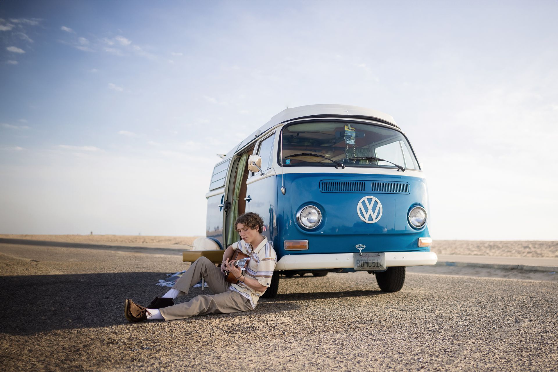 A man is sitting on the ground in front of a blue vw van.