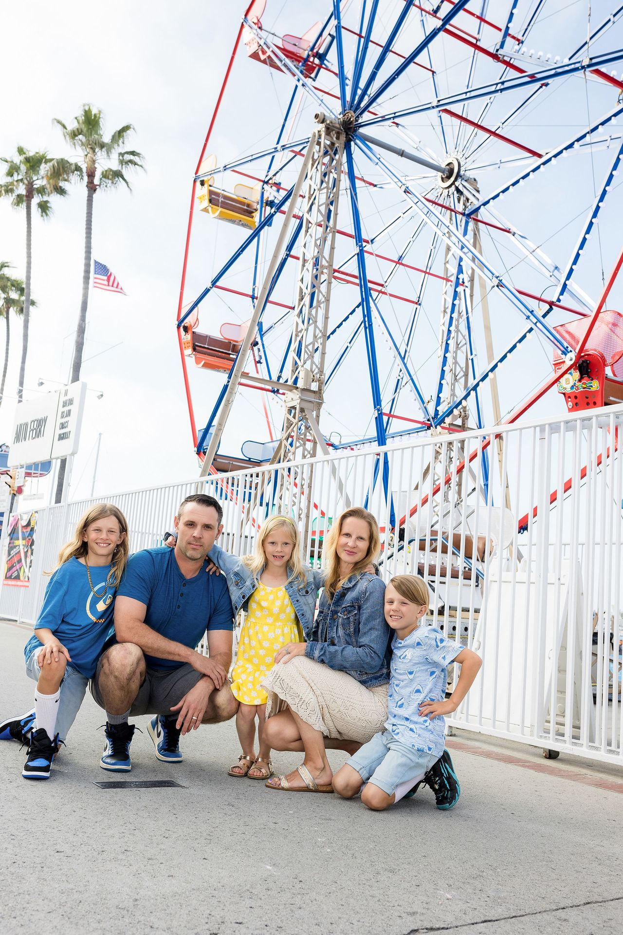 Family crouching in front of the Ferris wheel at the Balboa Fun Zone, Newport Beach