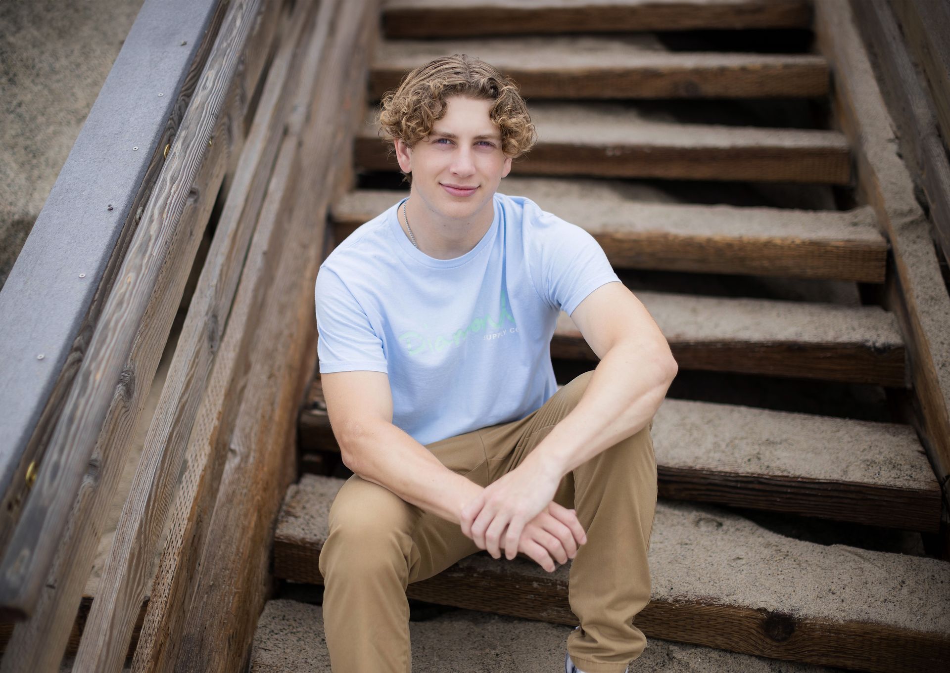 A young man is sitting on a set of wooden stairs.