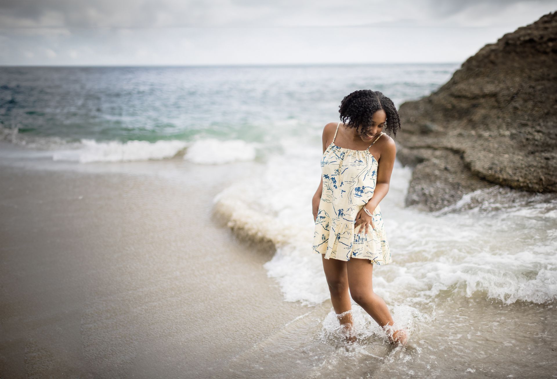 A woman in a dress is standing in the water on the beach.