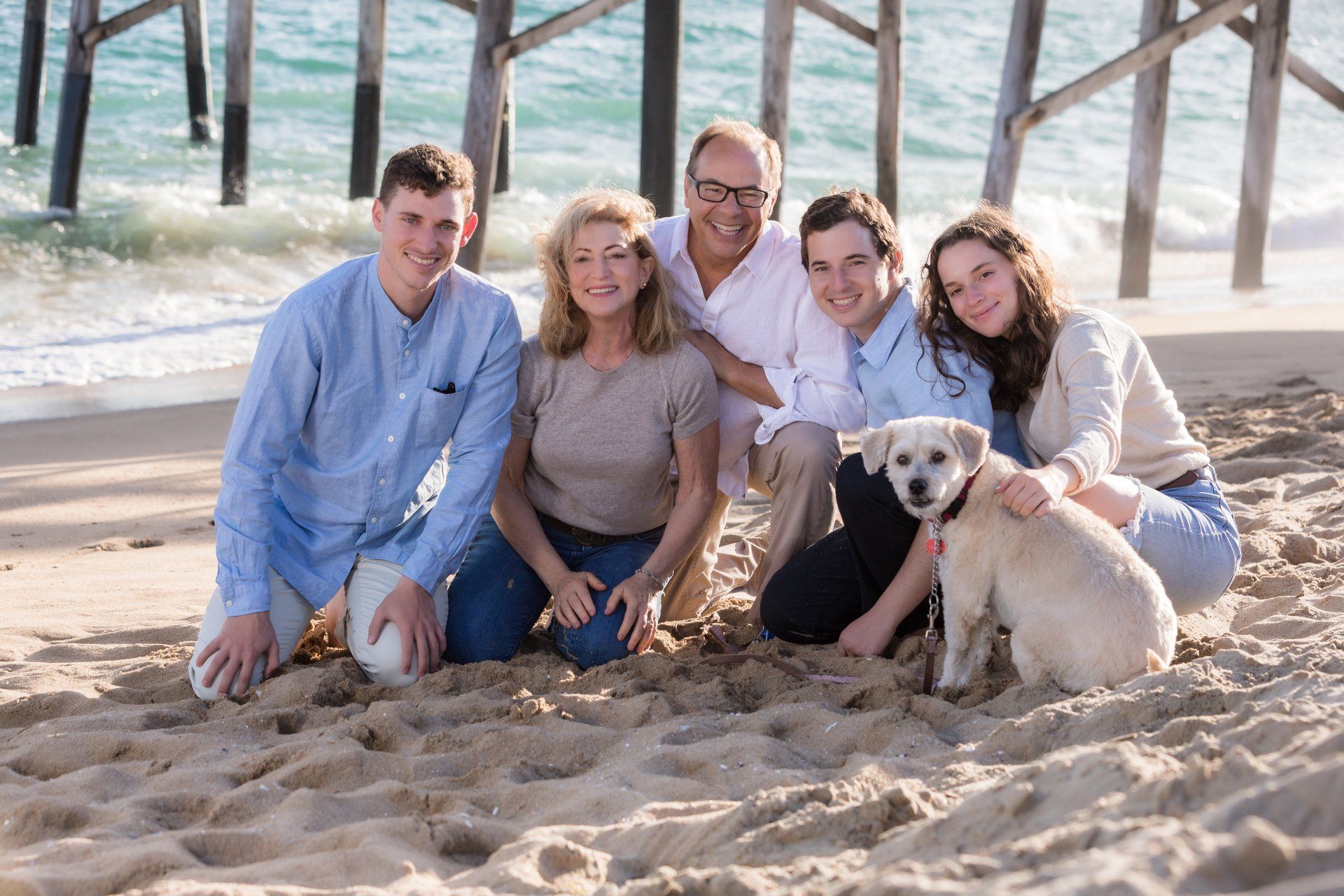 A family is posing for a picture on the beach with a dog.