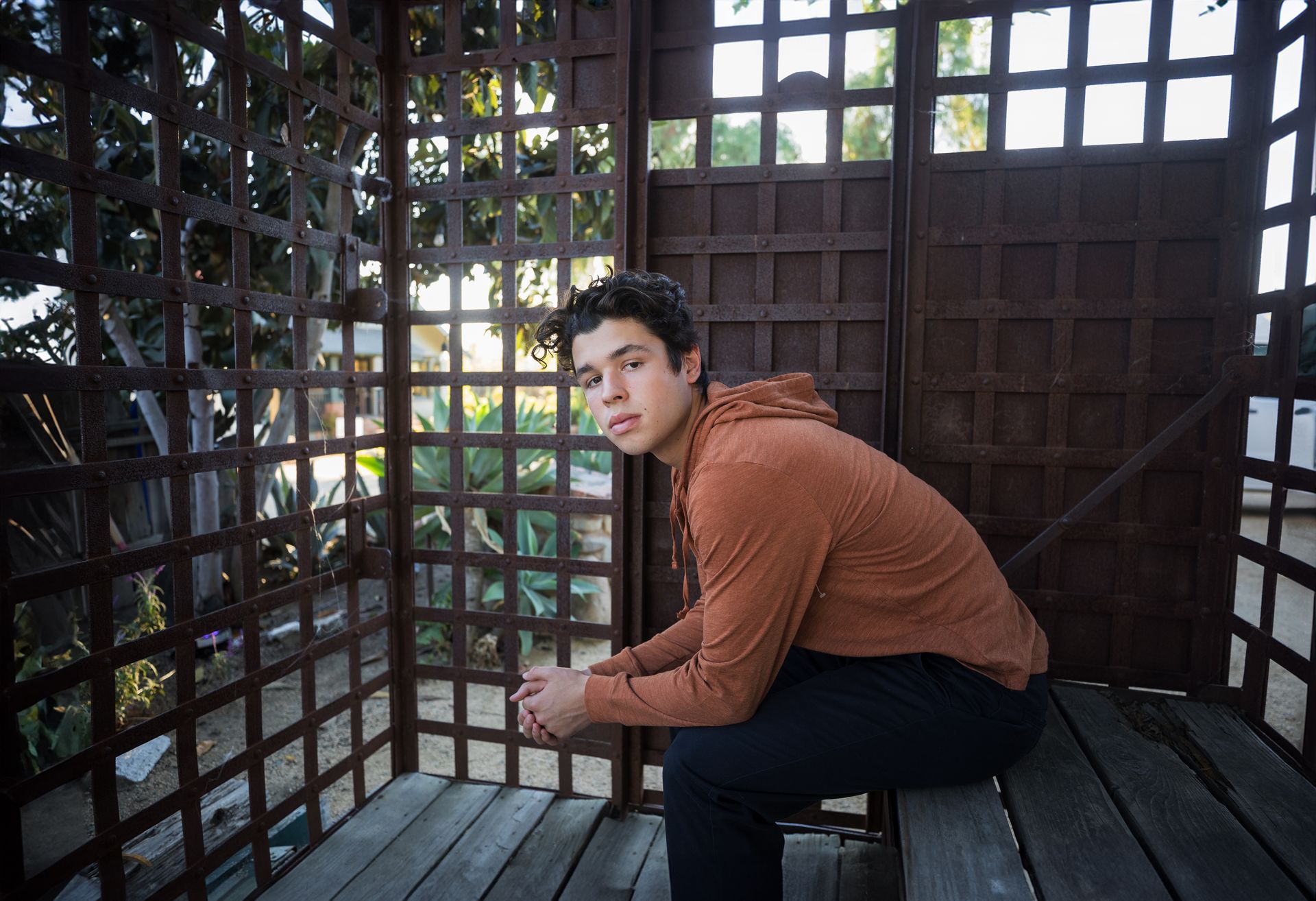 A young man is sitting on a wooden bench in front of a wooden fence.