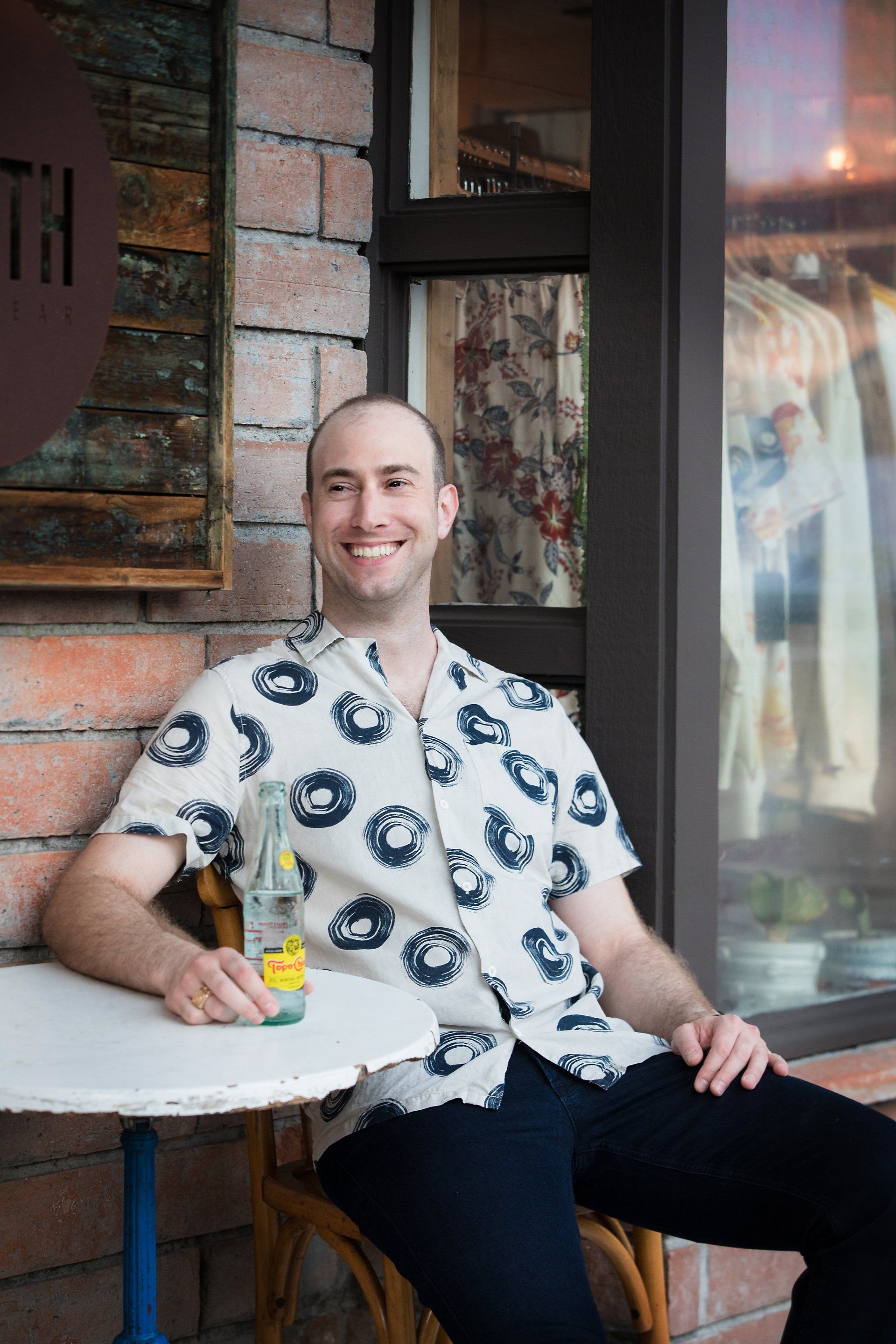 A man is sitting at a table with a bottle of soda.