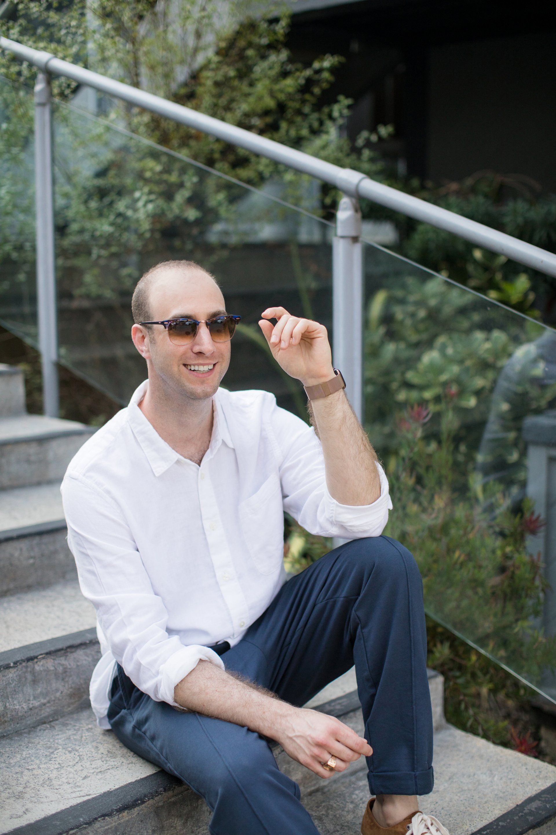 A man wearing sunglasses is sitting on a set of stairs.