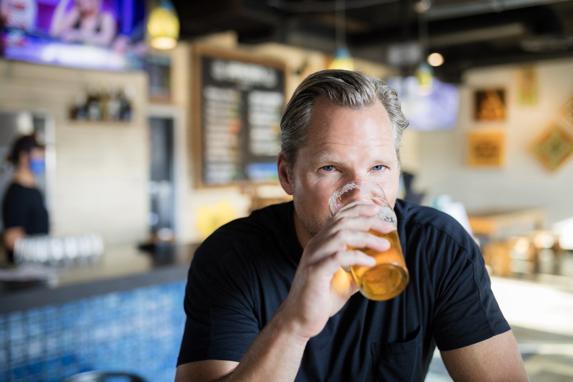 A man is drinking a glass of beer in a restaurant.