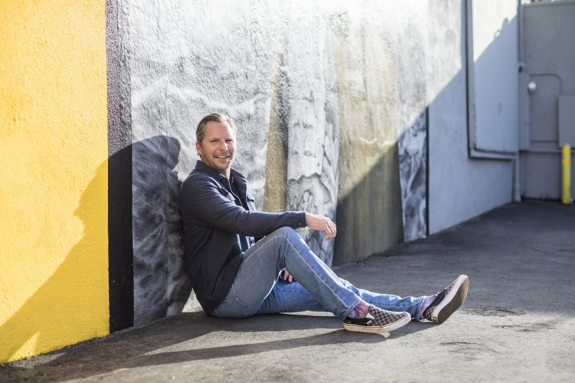 A man is sitting on the ground leaning against a wall.