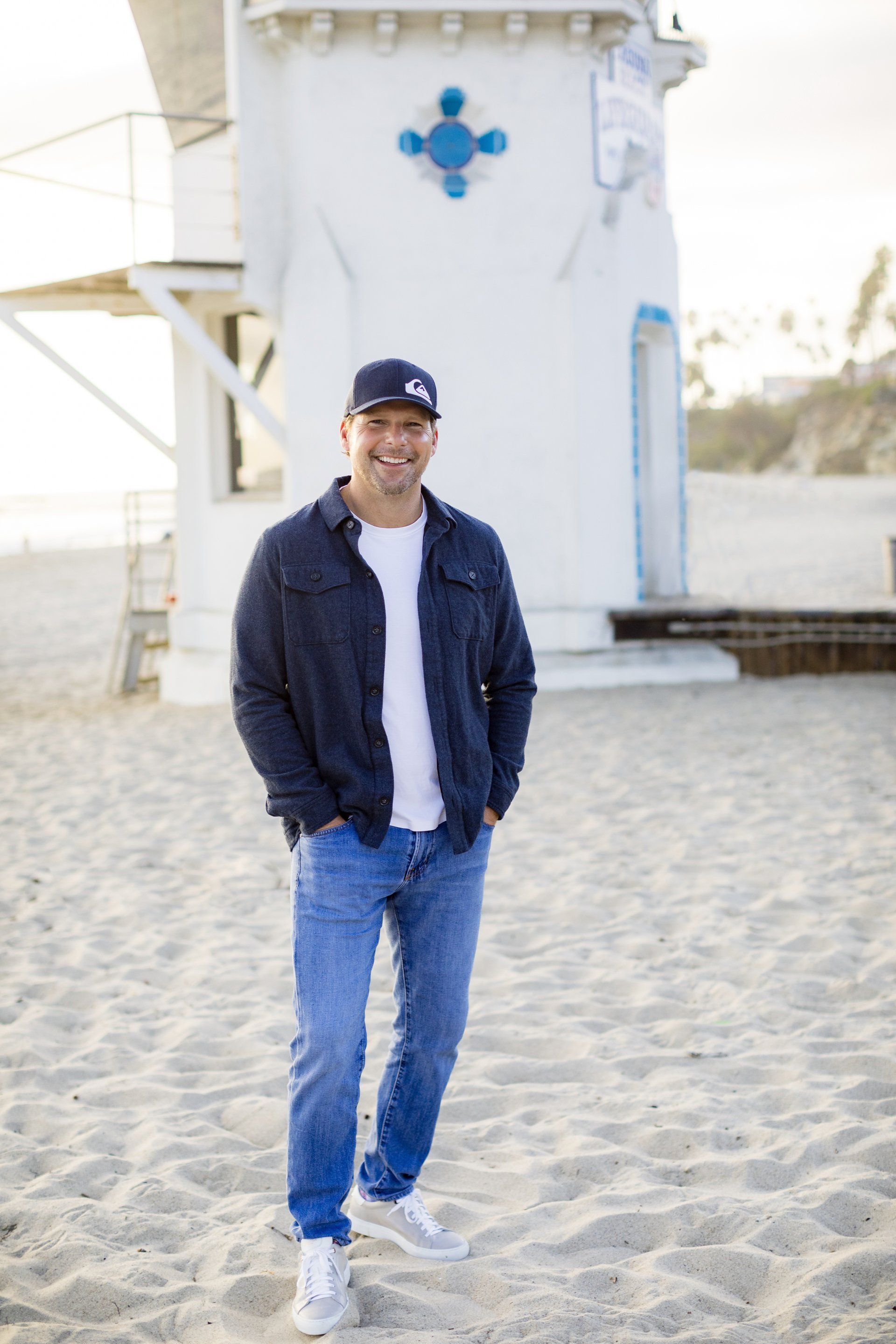 A man is standing on a beach in front of a lifeguard tower.