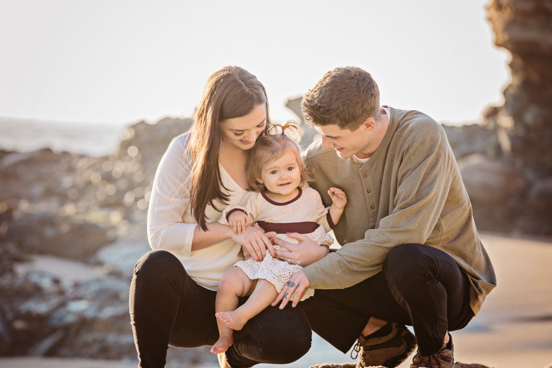 A man and woman are kneeling down with a baby on the beach.