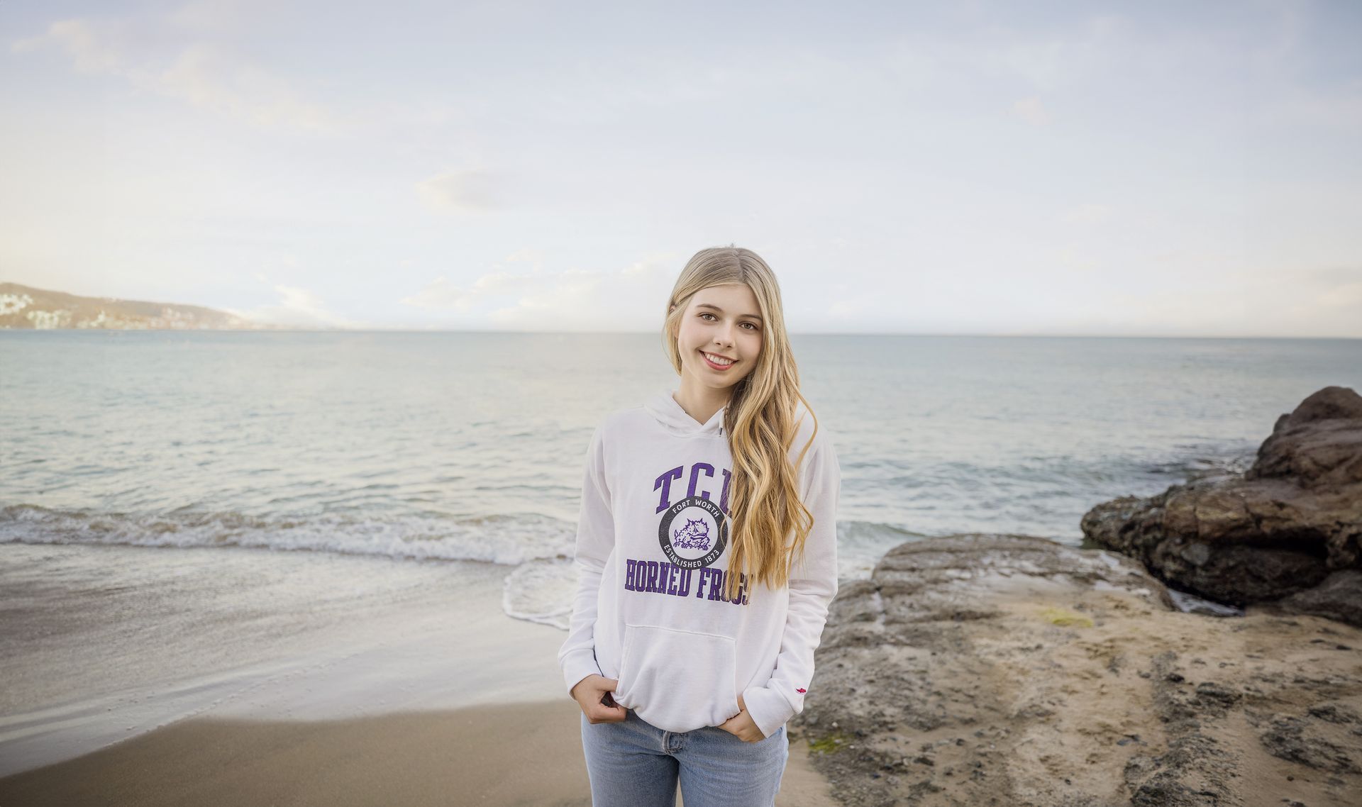 A young girl is standing on a beach with her hands in her pockets.