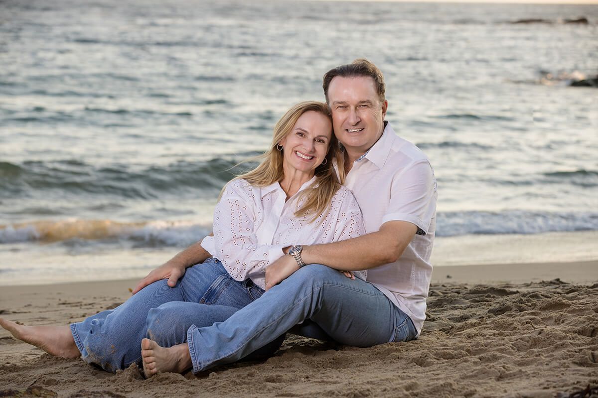 Couple sitting on the sand at Laguna Beach during sunset, smiling and embracing