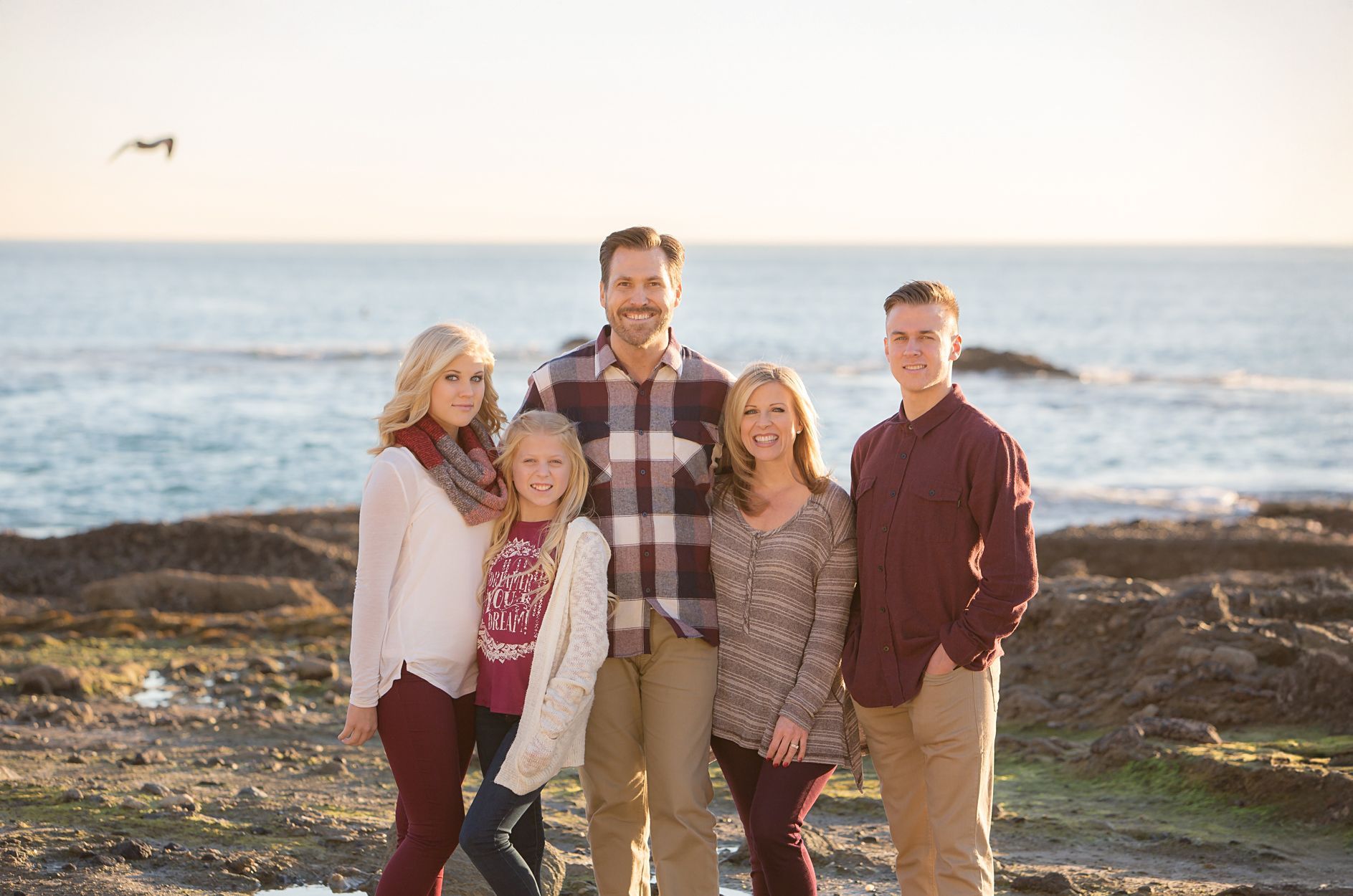 Five people standing on a rocky beach at sunset, smiling toward the camera.