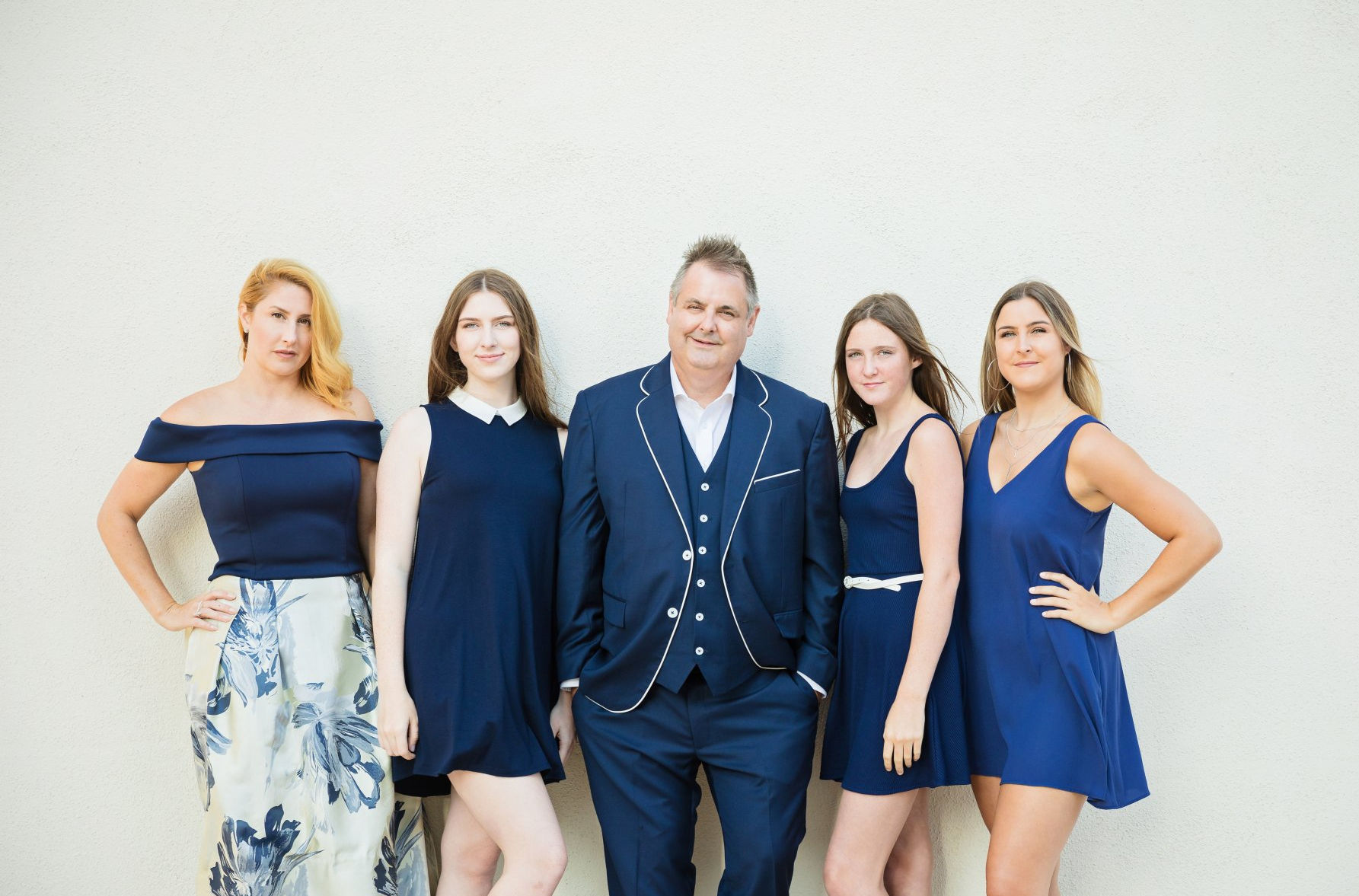 A man in a suit is standing next to three women in blue dresses.