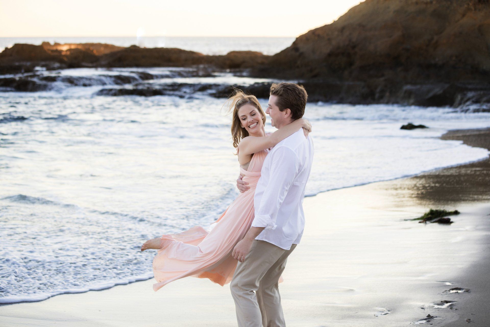 A man is holding a woman in his arms on the beach.