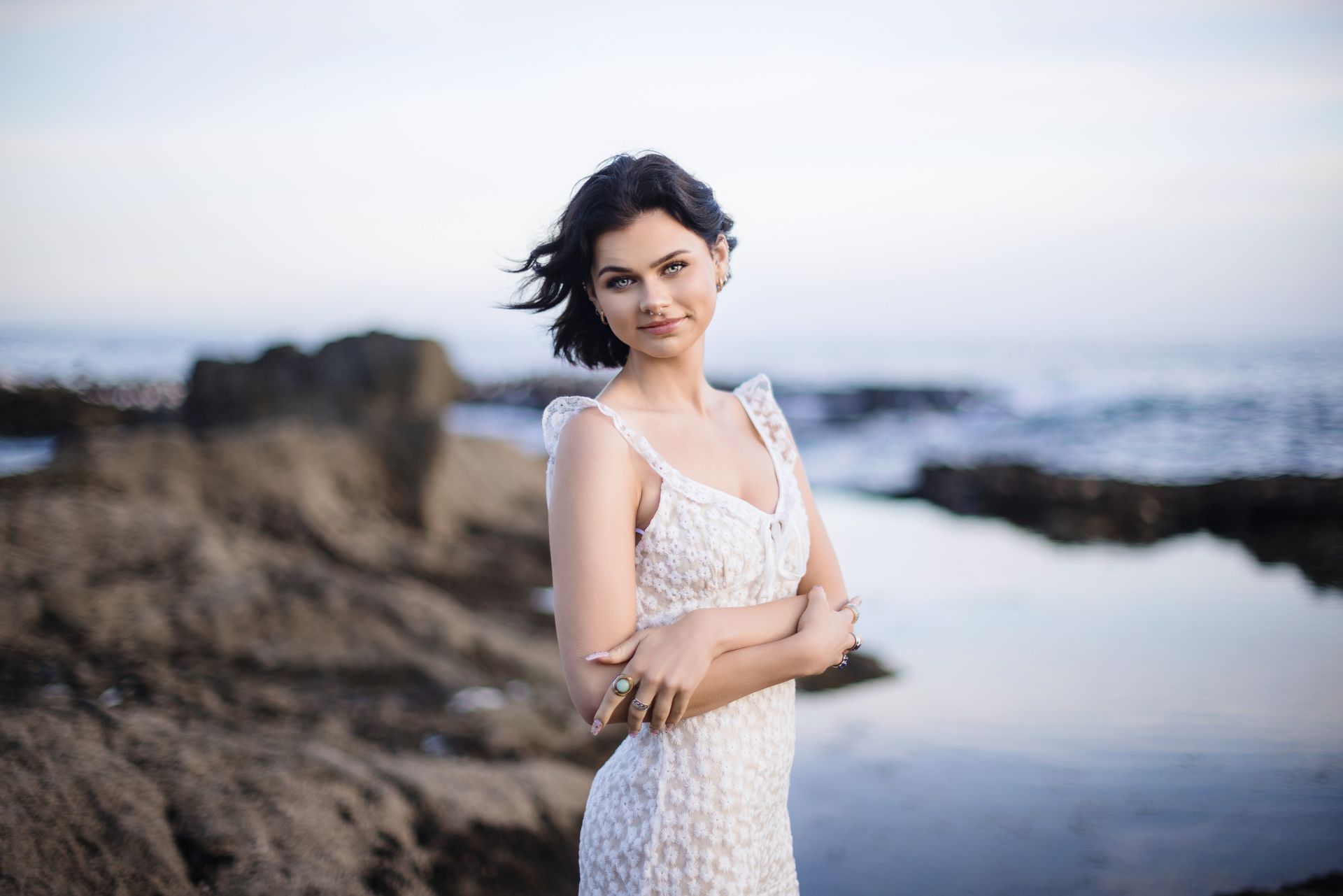 A woman in a white dress is standing on a rocky beach.