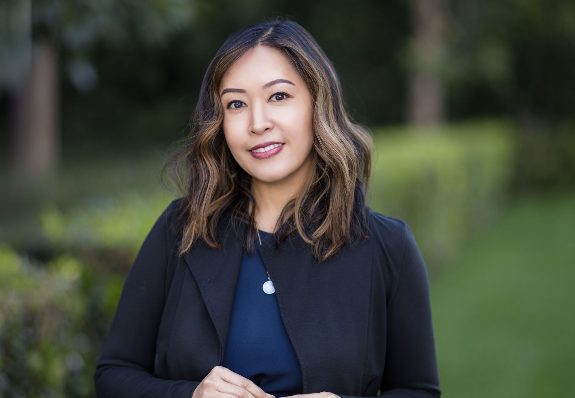 A woman in a black jacket and blue shirt is standing in a park.