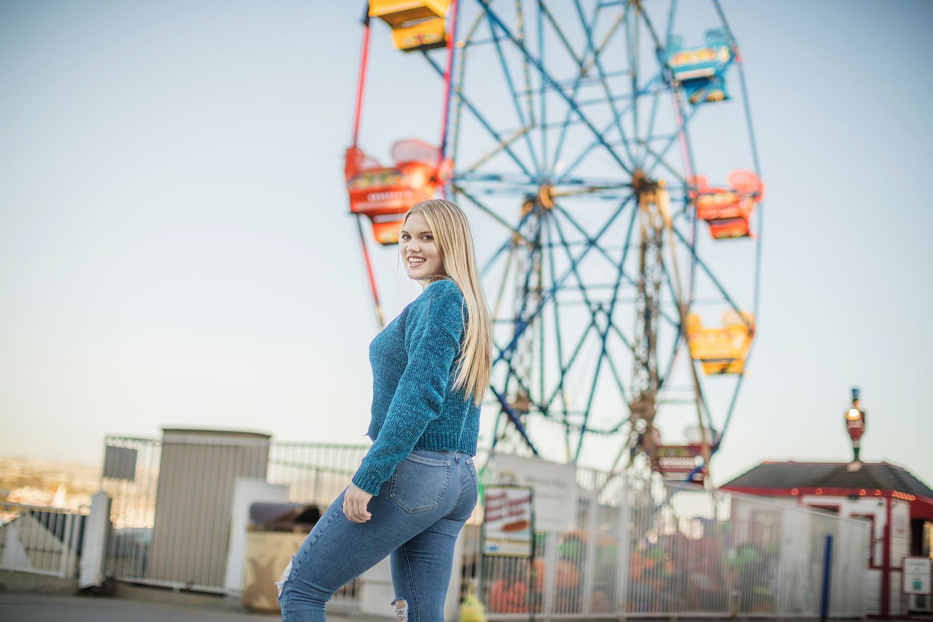 A woman is standing in front of a ferris wheel at an amusement park.