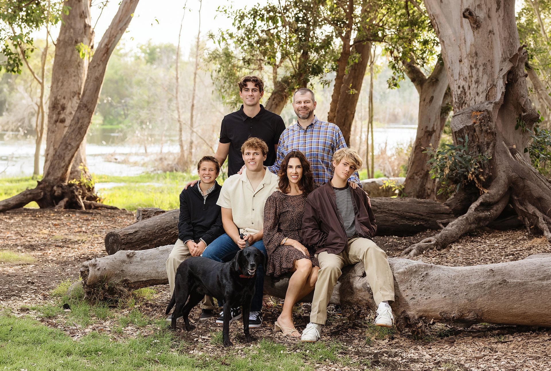 Family and their black lab on a fallen log in the Huntington Beach Urban Forest