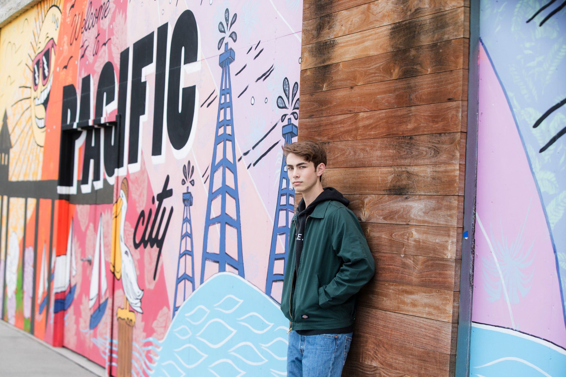 A young man is leaning against a wall with graffiti on it.