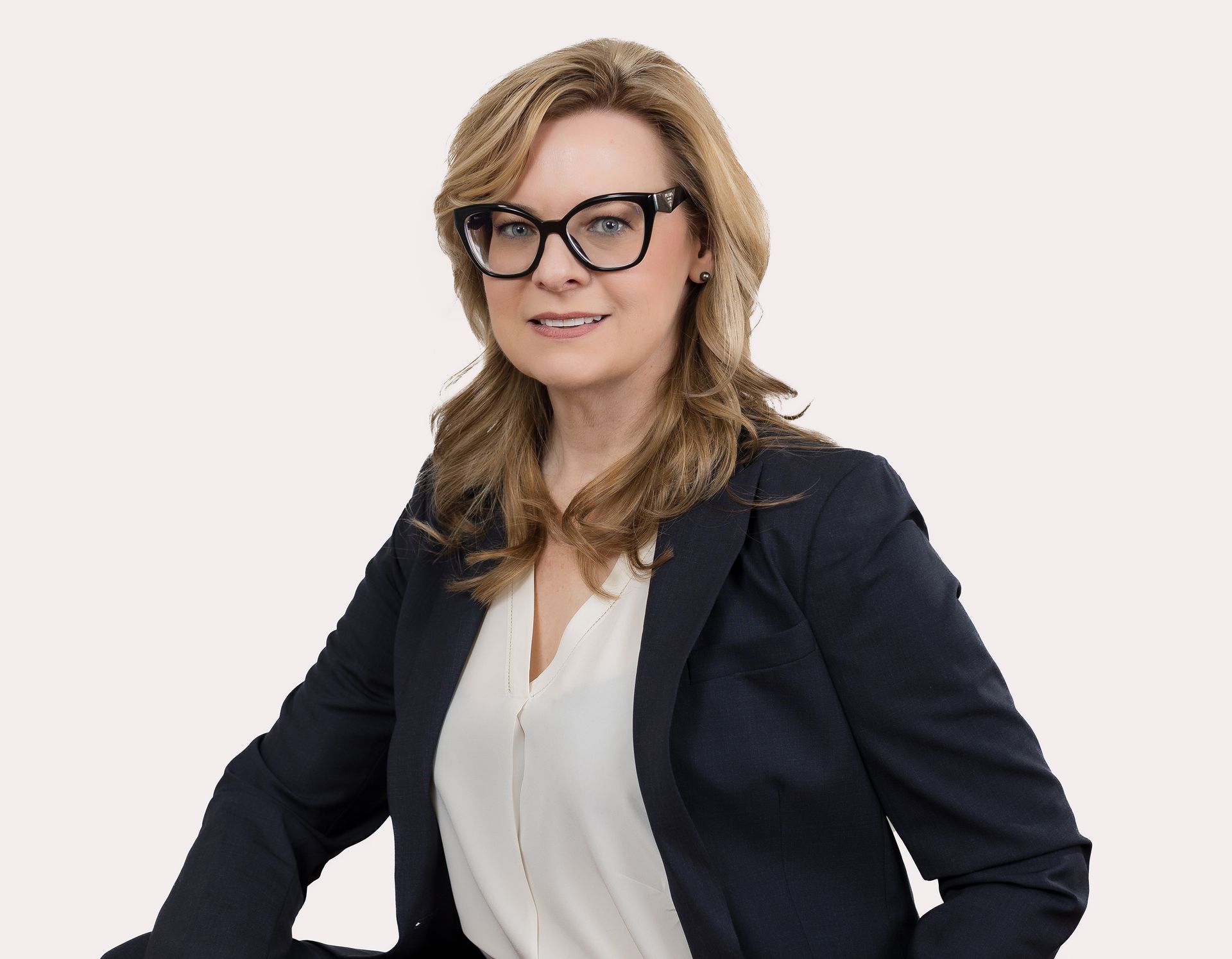 A woman wearing glasses and a black jacket is sitting on a chair.