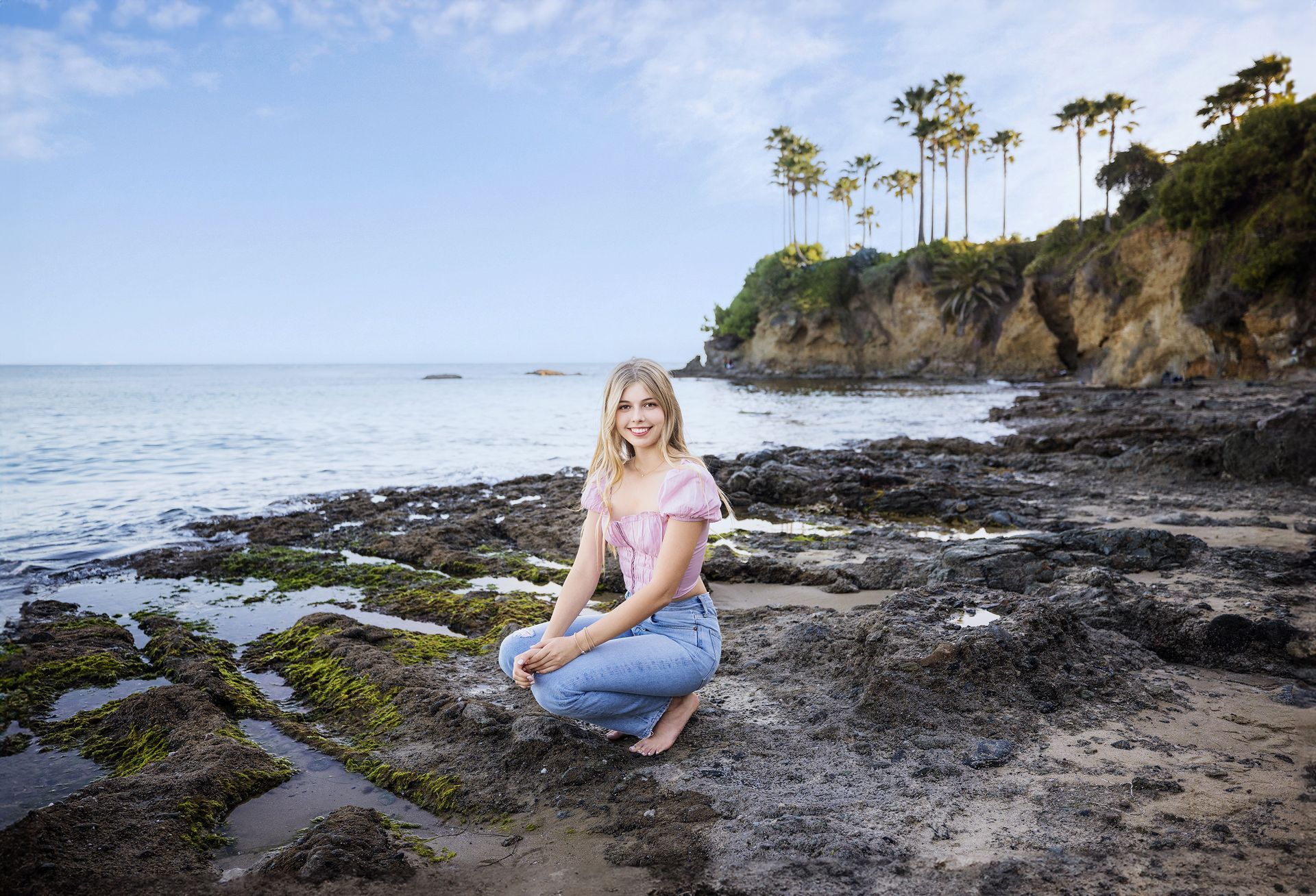 A woman is kneeling on a rocky beach near the ocean.