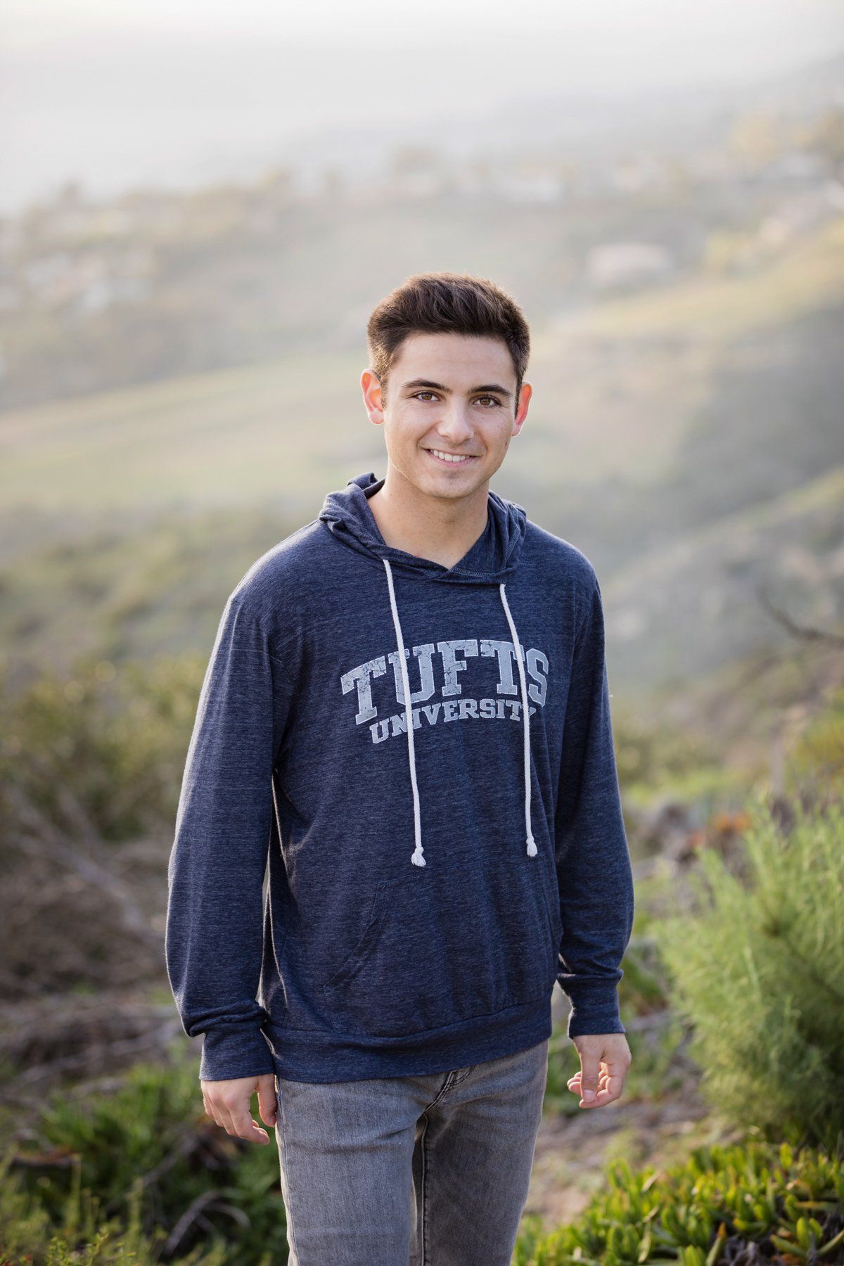 A young man wearing a blue hoodie is standing on top of a hill.