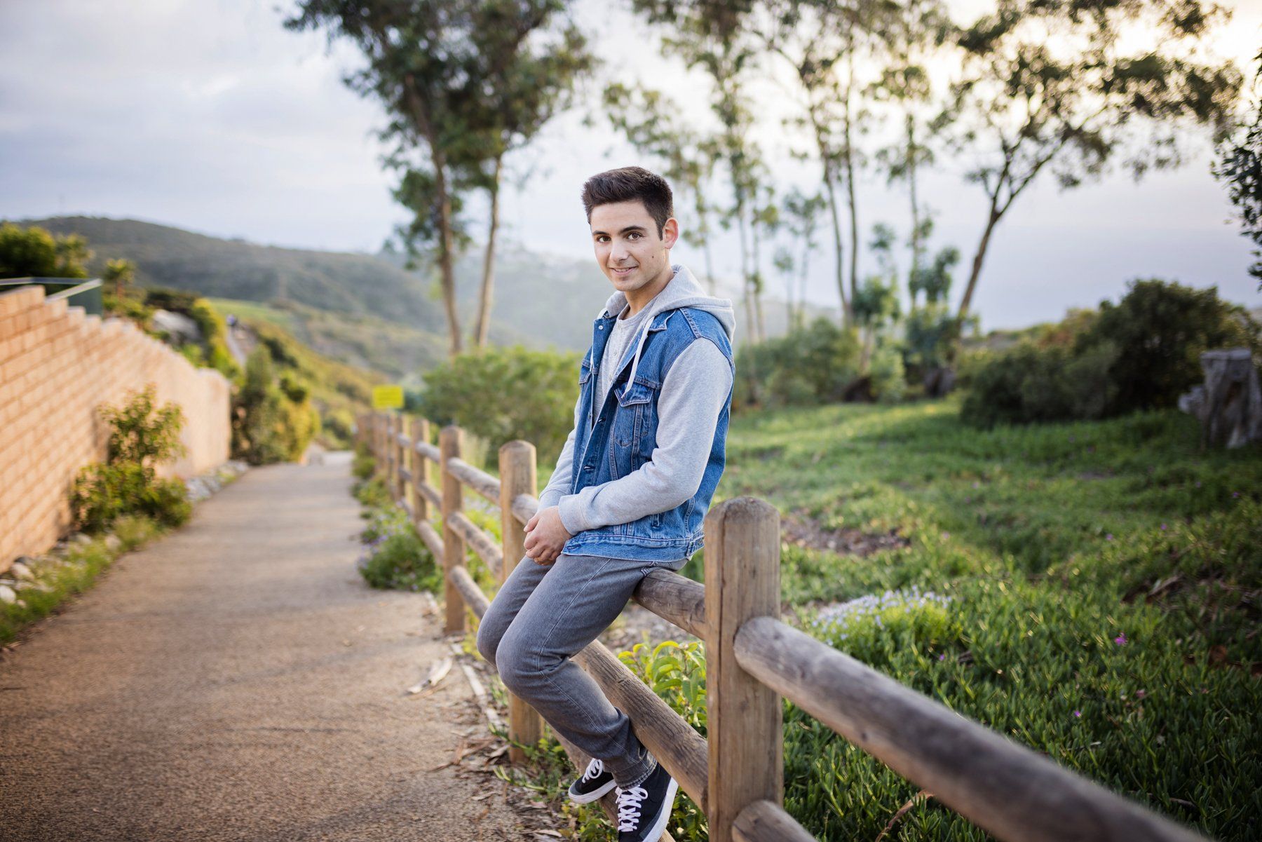 A young man is sitting on a wooden fence.