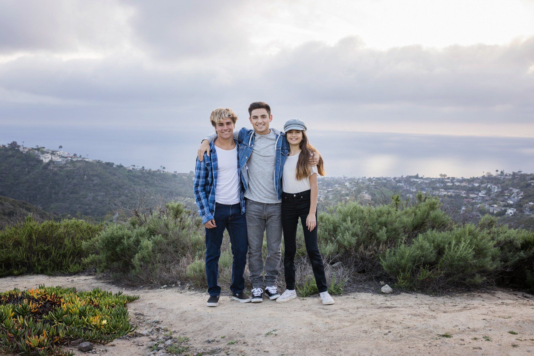 Three young people are posing for a picture on top of a hill.