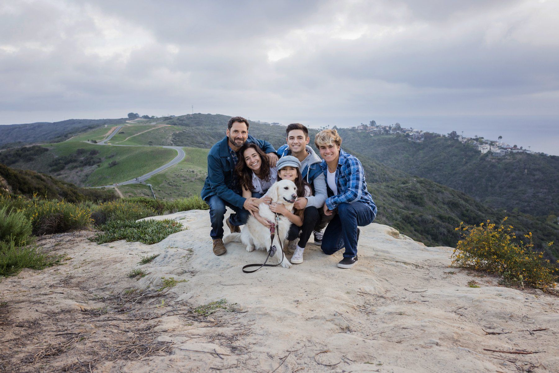 Family photo in Laguna Beach A family is posing for a picture with their dog on top of a hill.