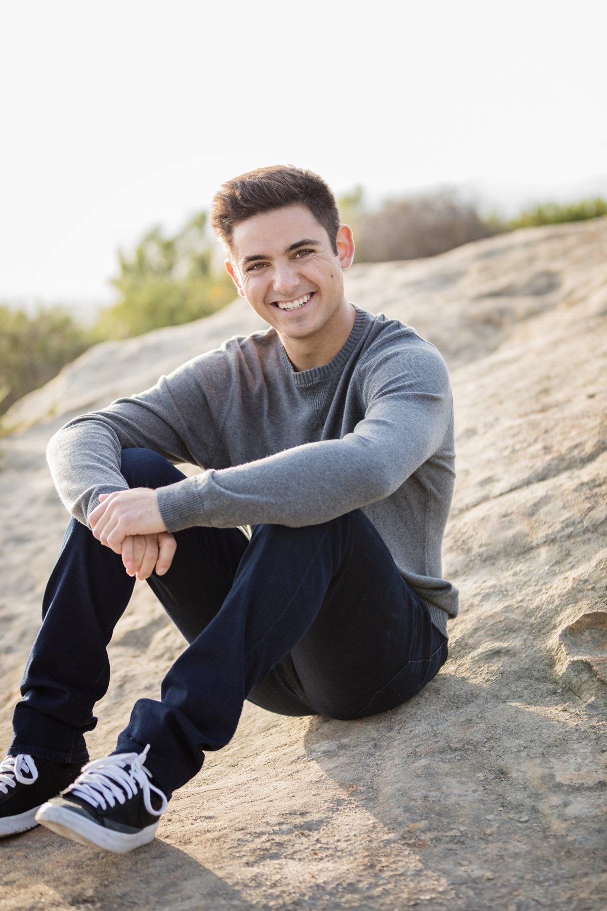 A young man is sitting on a rock and smiling.