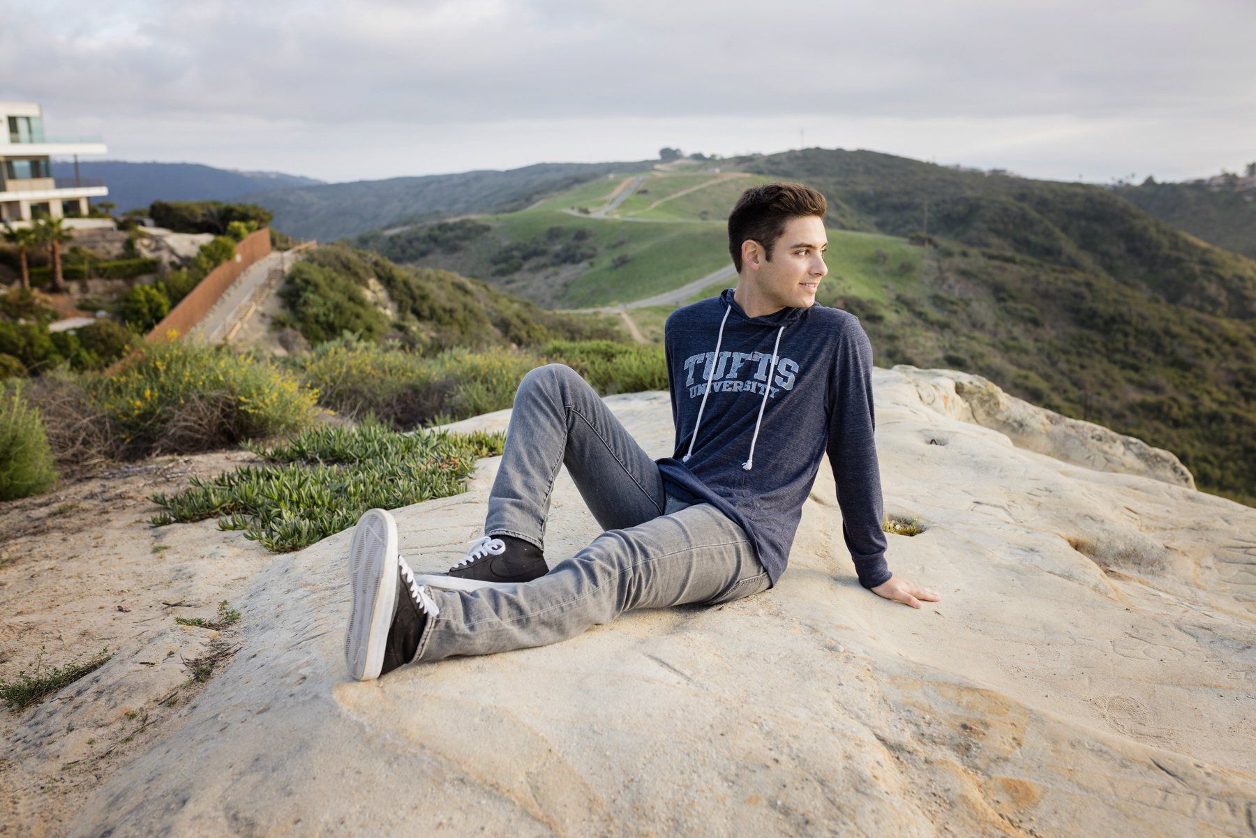 A young man is sitting on top of a rocky hill.