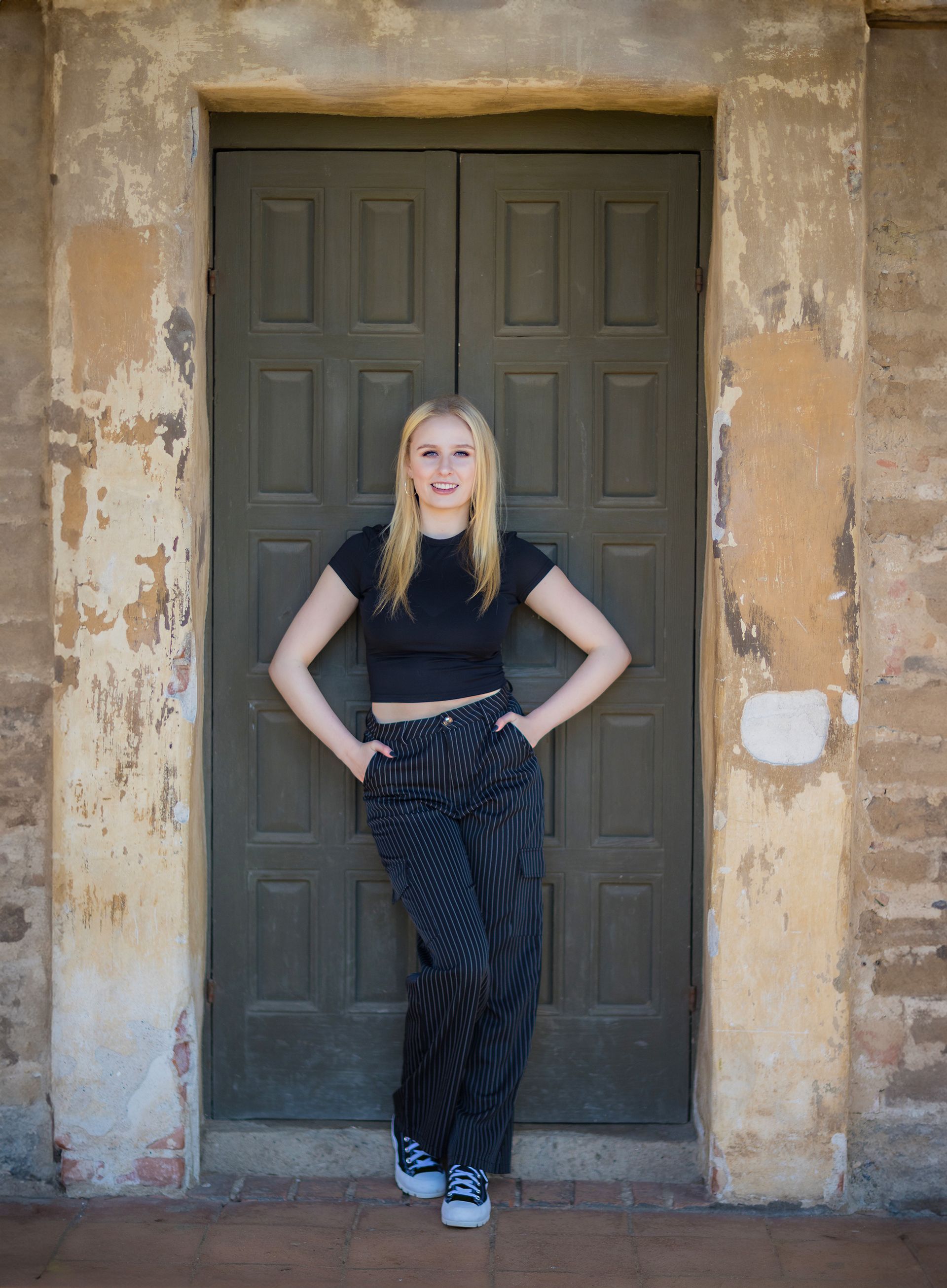 A woman is standing in front of a door with her hands in her pockets.