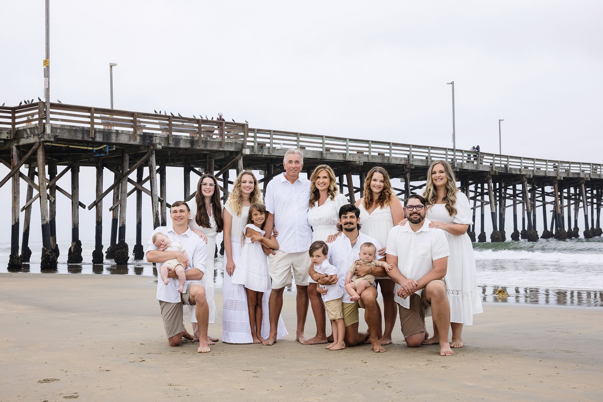 Extended family in white on the sand beside the Newport Beach Pier