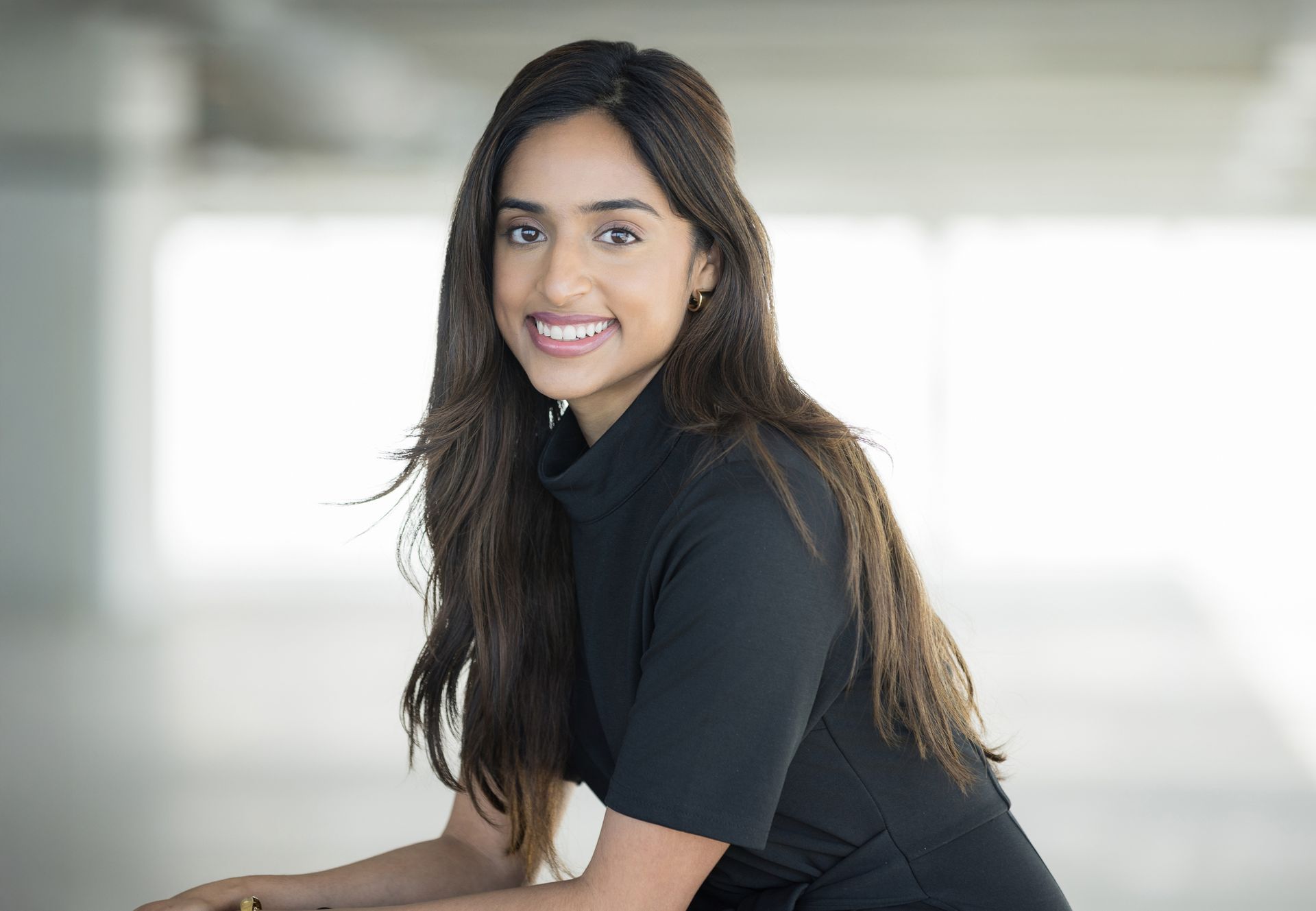 Smiling person in a black shirt leaning forward against a bright, blurred background