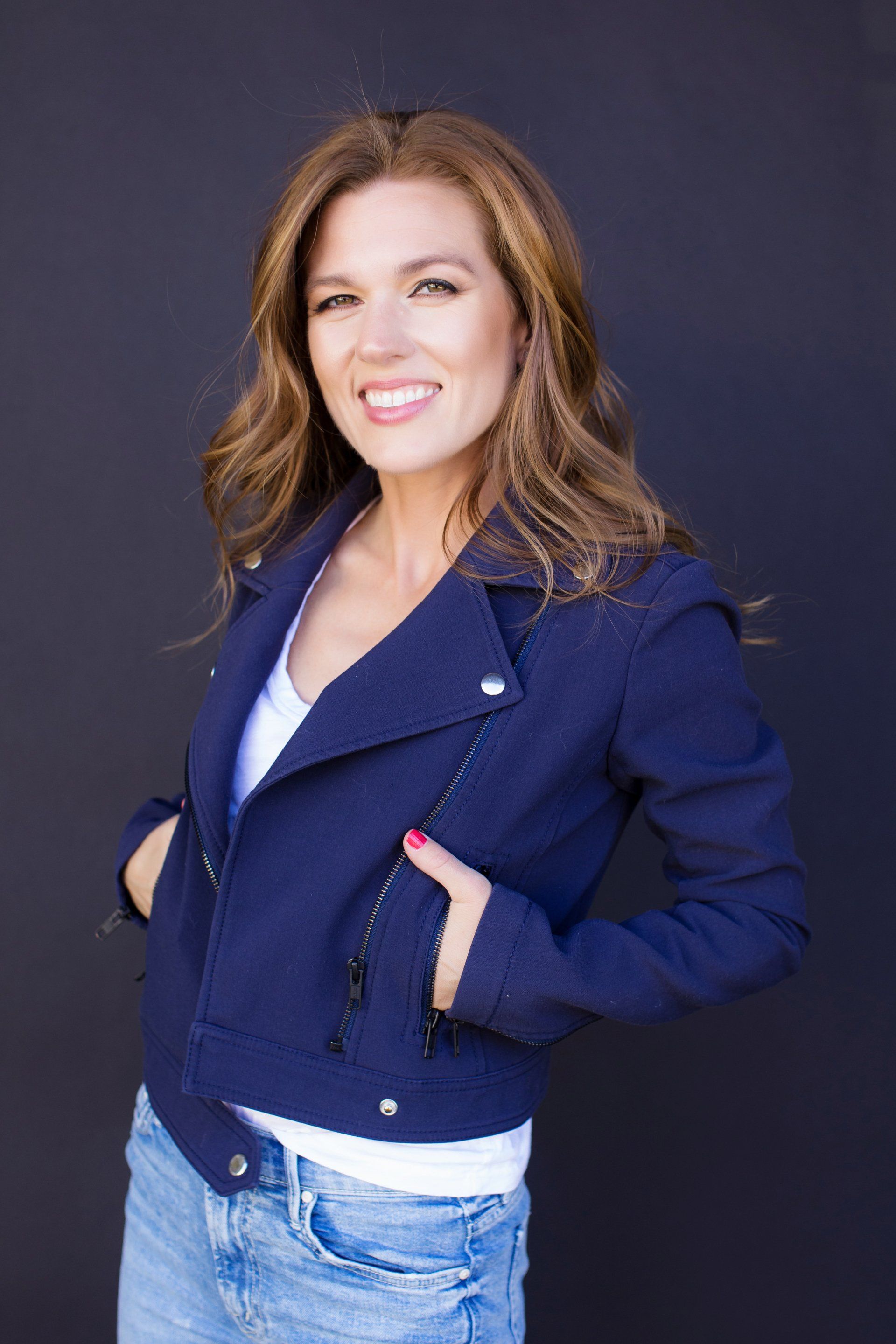 Confident coach headshot in a navy jacket on a dark backdrop