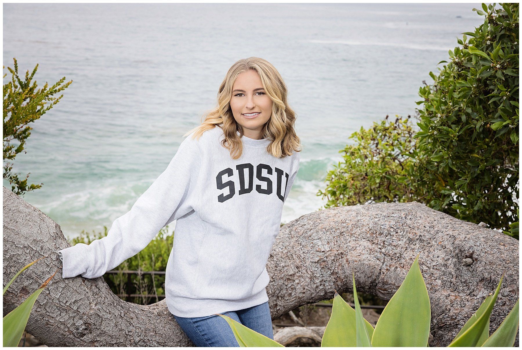A woman in a sweatshirt is sitting on a rock near the ocean.