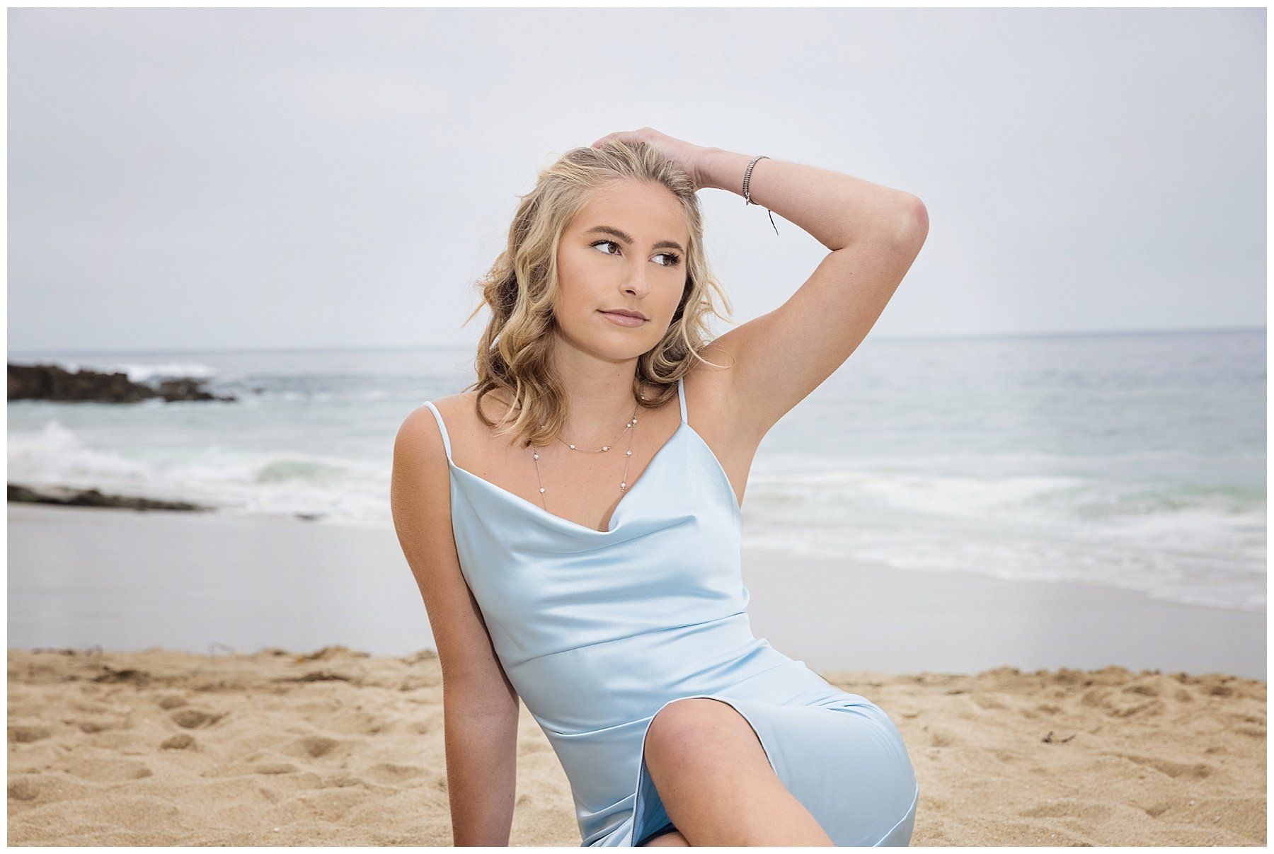 A woman in a blue dress is sitting on the beach.