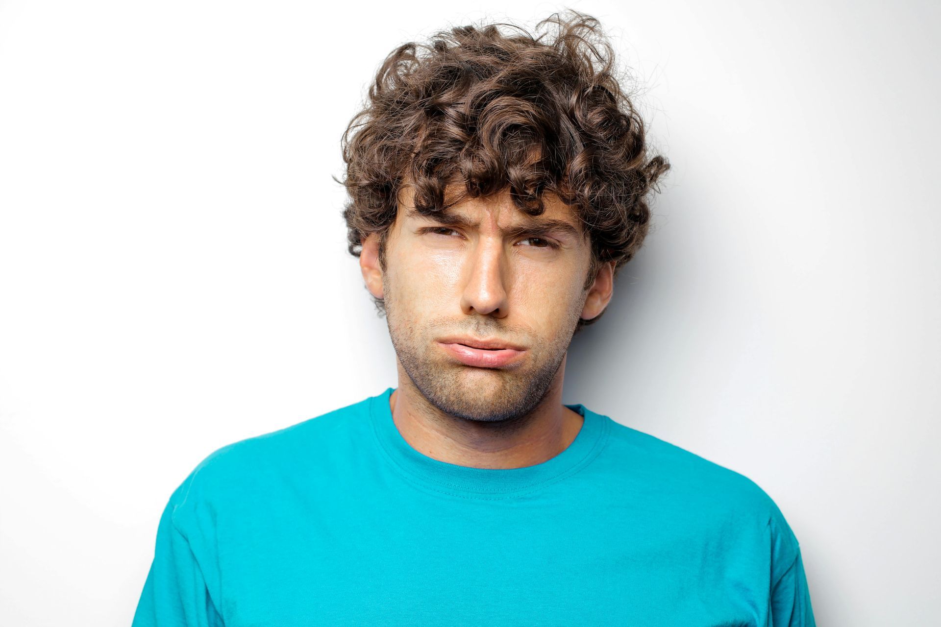 A man with curly hair is wearing a blue shirt and making a funny face.