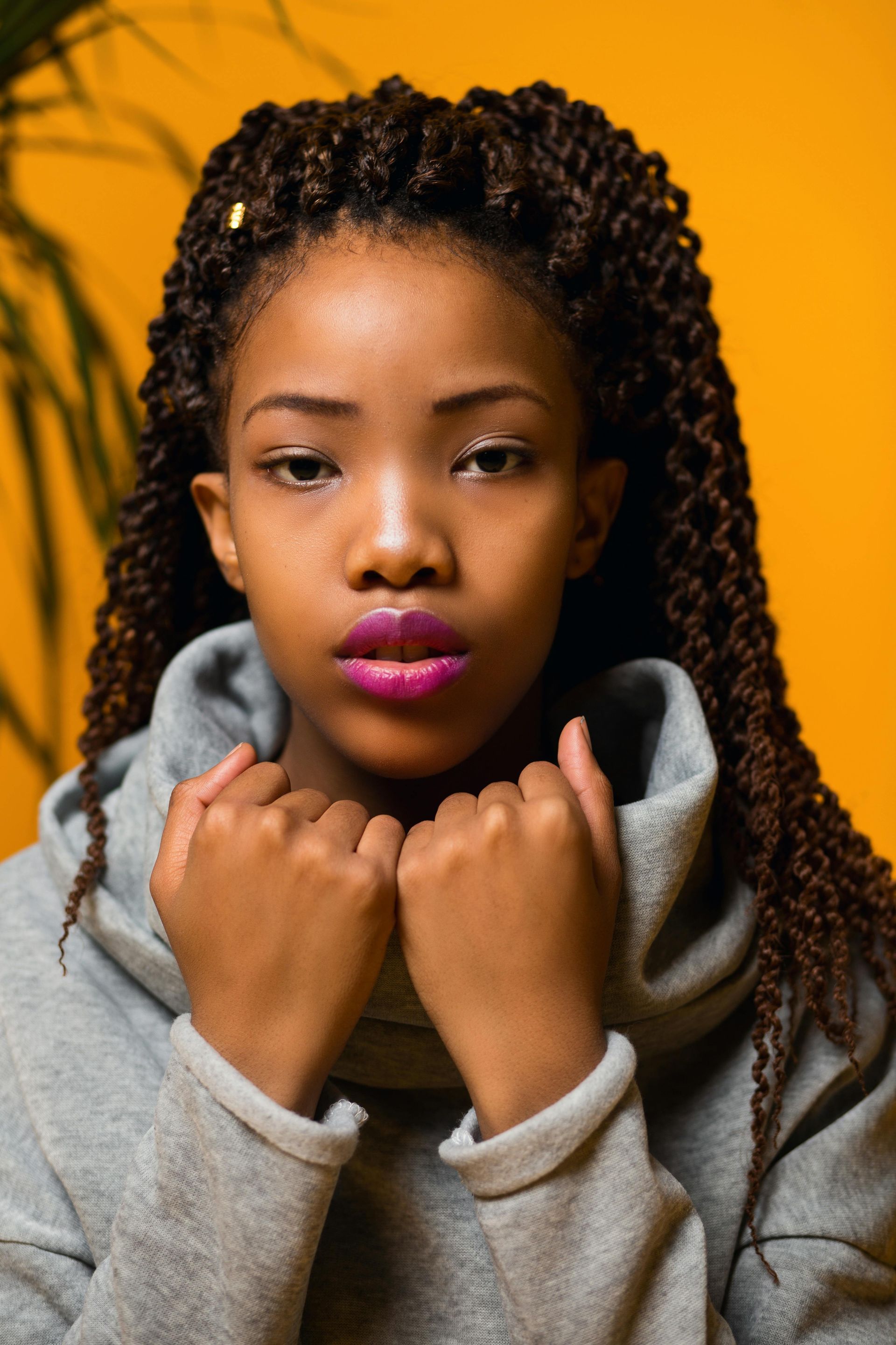 A young woman with braids is wearing a gray sweater and pink lipstick.