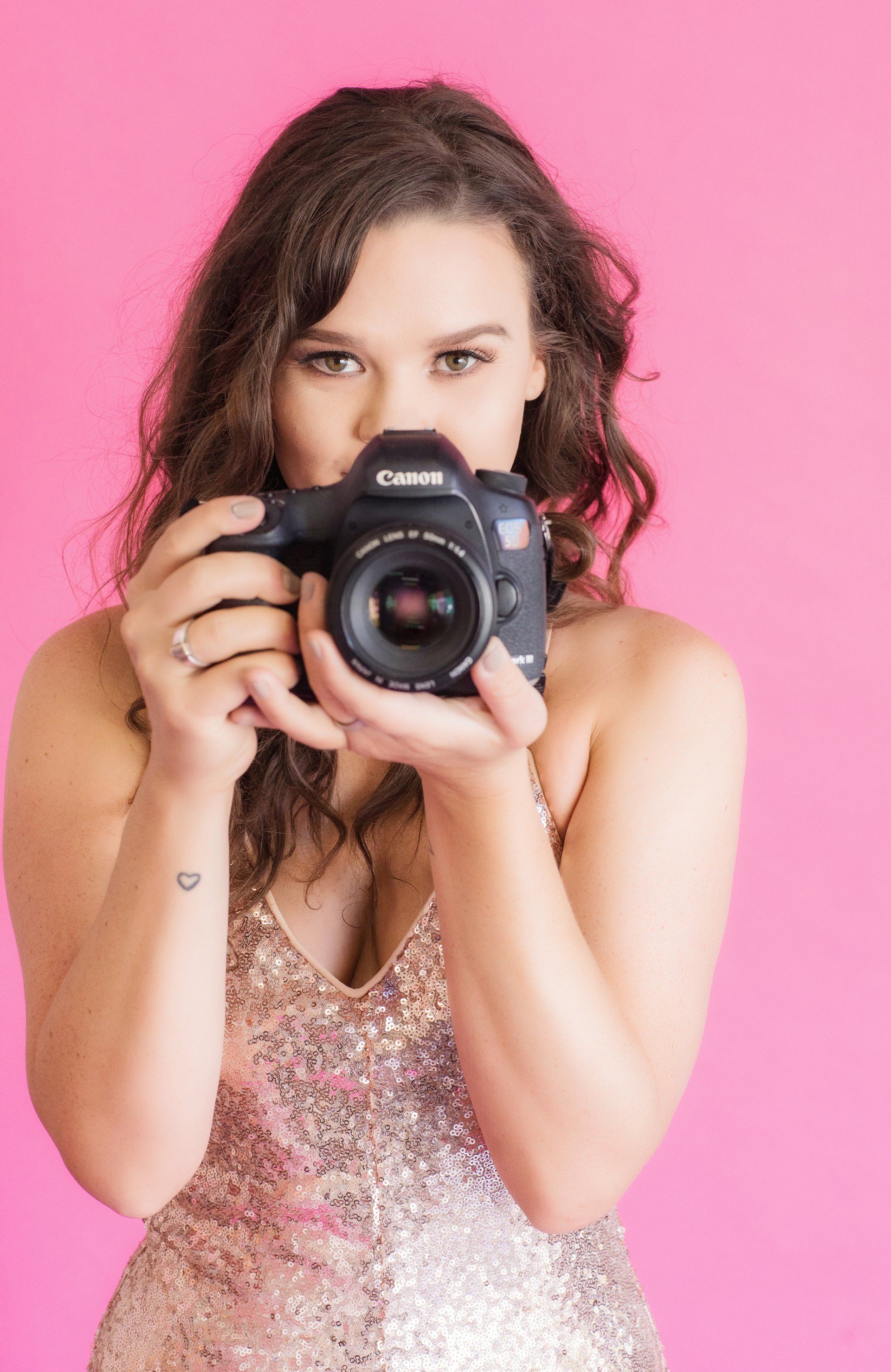 Photographer headshot holding a camera against a pink backdrop