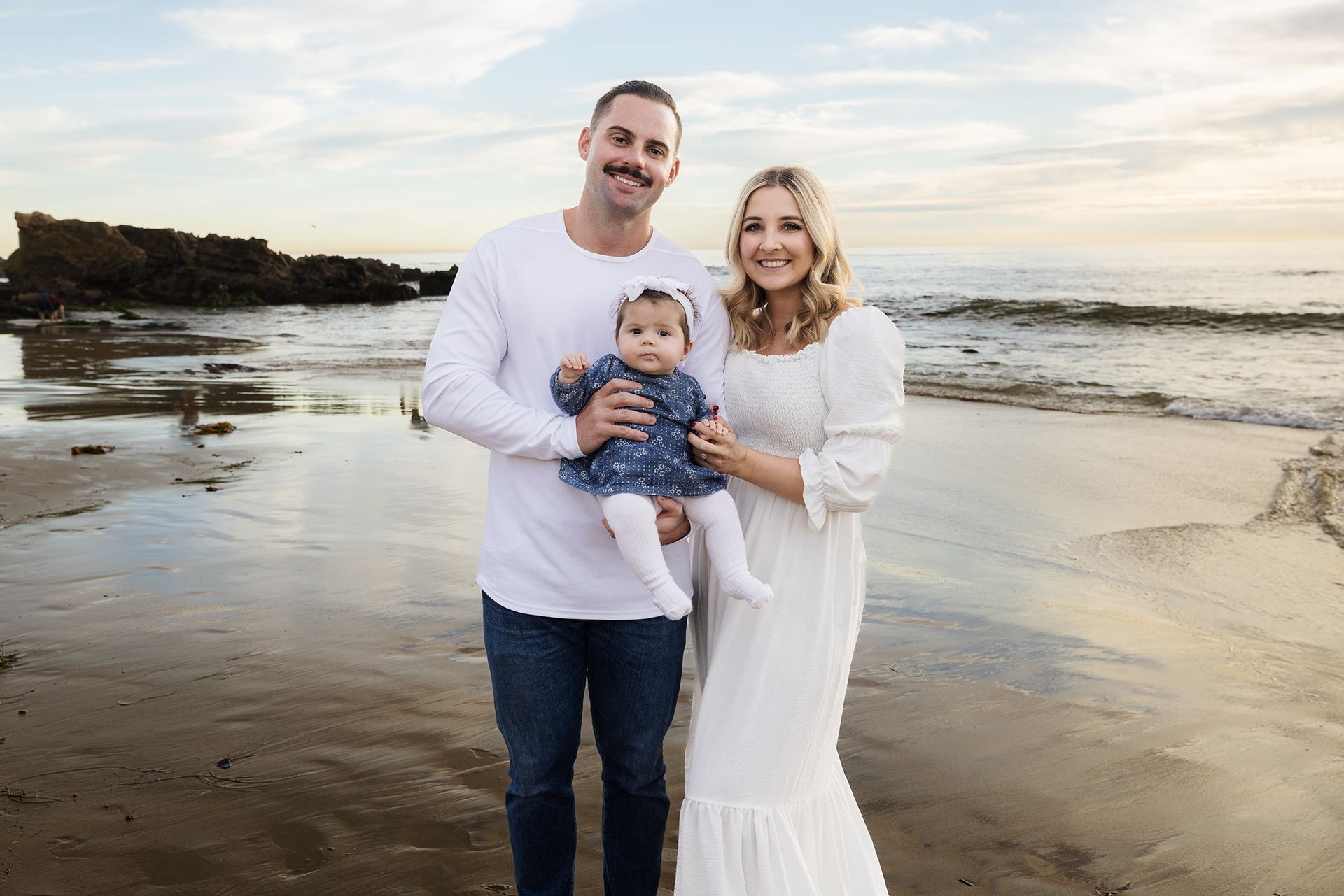 Young parents with their baby on the shoreline during an extended family session in Laguna Beach