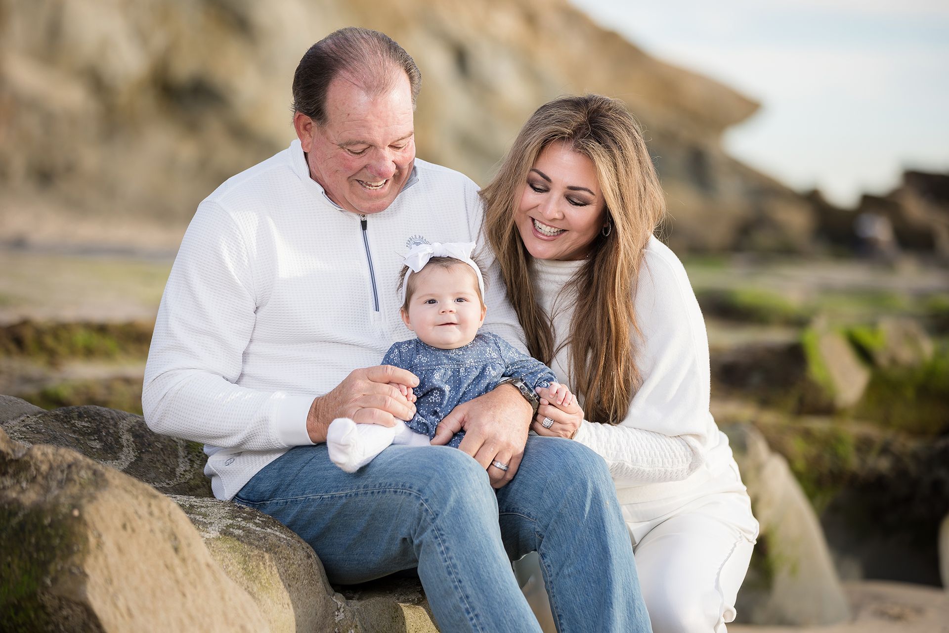 Grandfather and daughter with the newest grandchild on the rocks in Laguna Beach