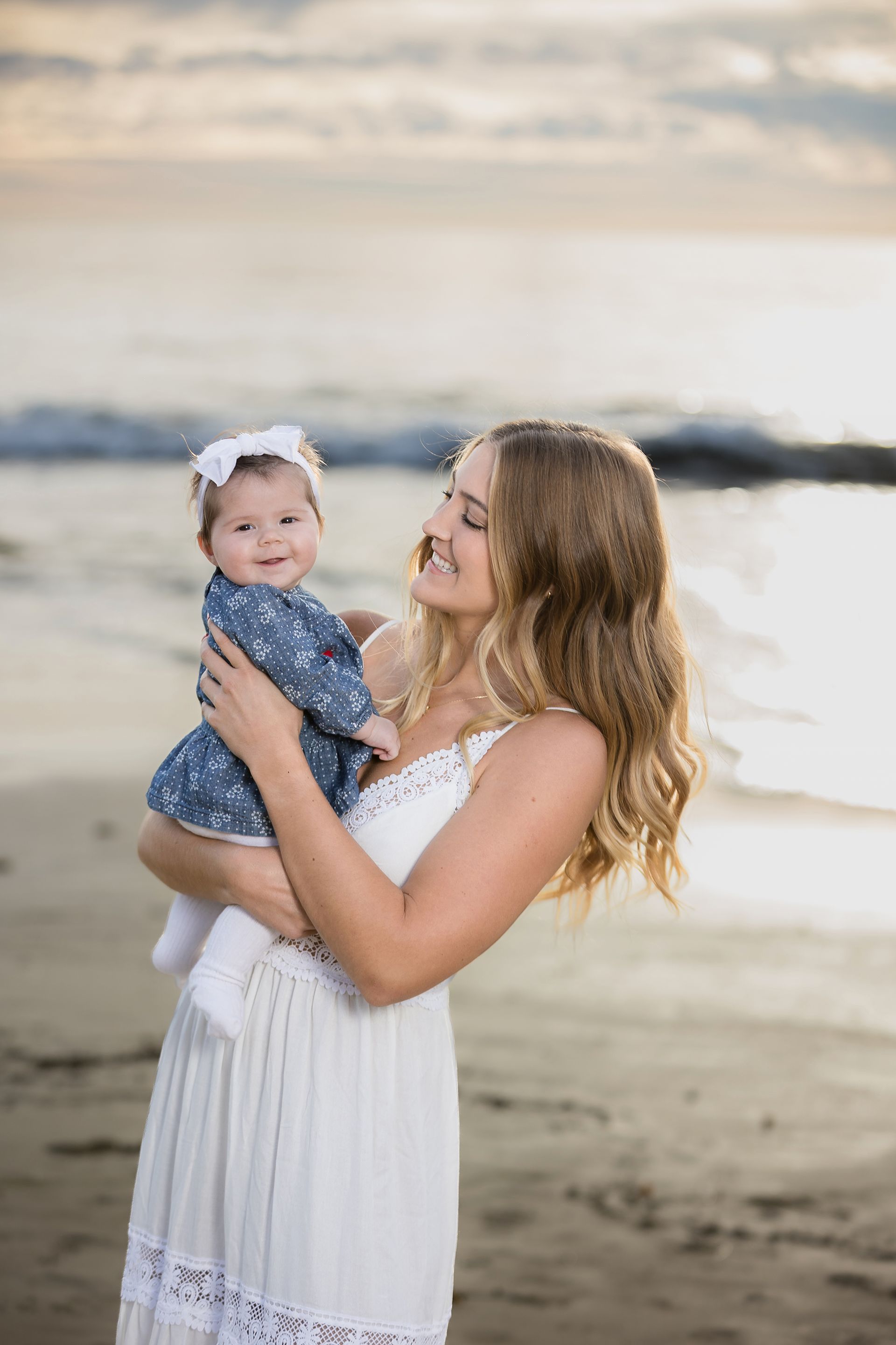 Mother holding her baby daughter at sunset on the beach in Laguna Beach during an extended family session