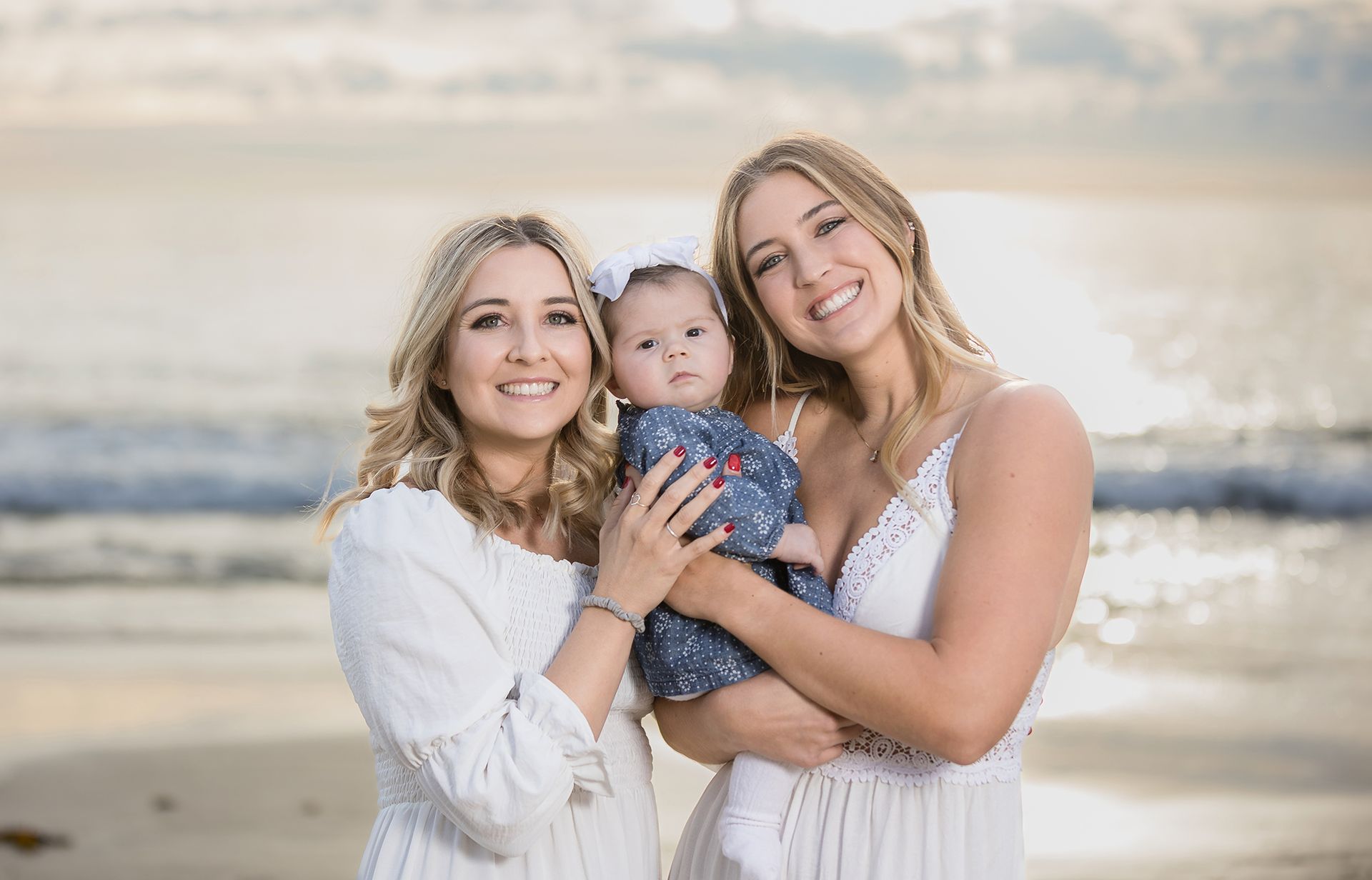 Mom and aunt posing with a 3 month old baby girl on the beach at sunset in Laguna Beach.