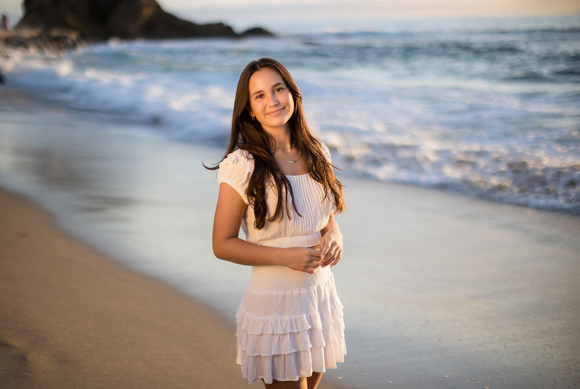 Teenage girl in a white dress walking barefoot along the shore during a Laguna Beach family session by a top Orange County family photographer.