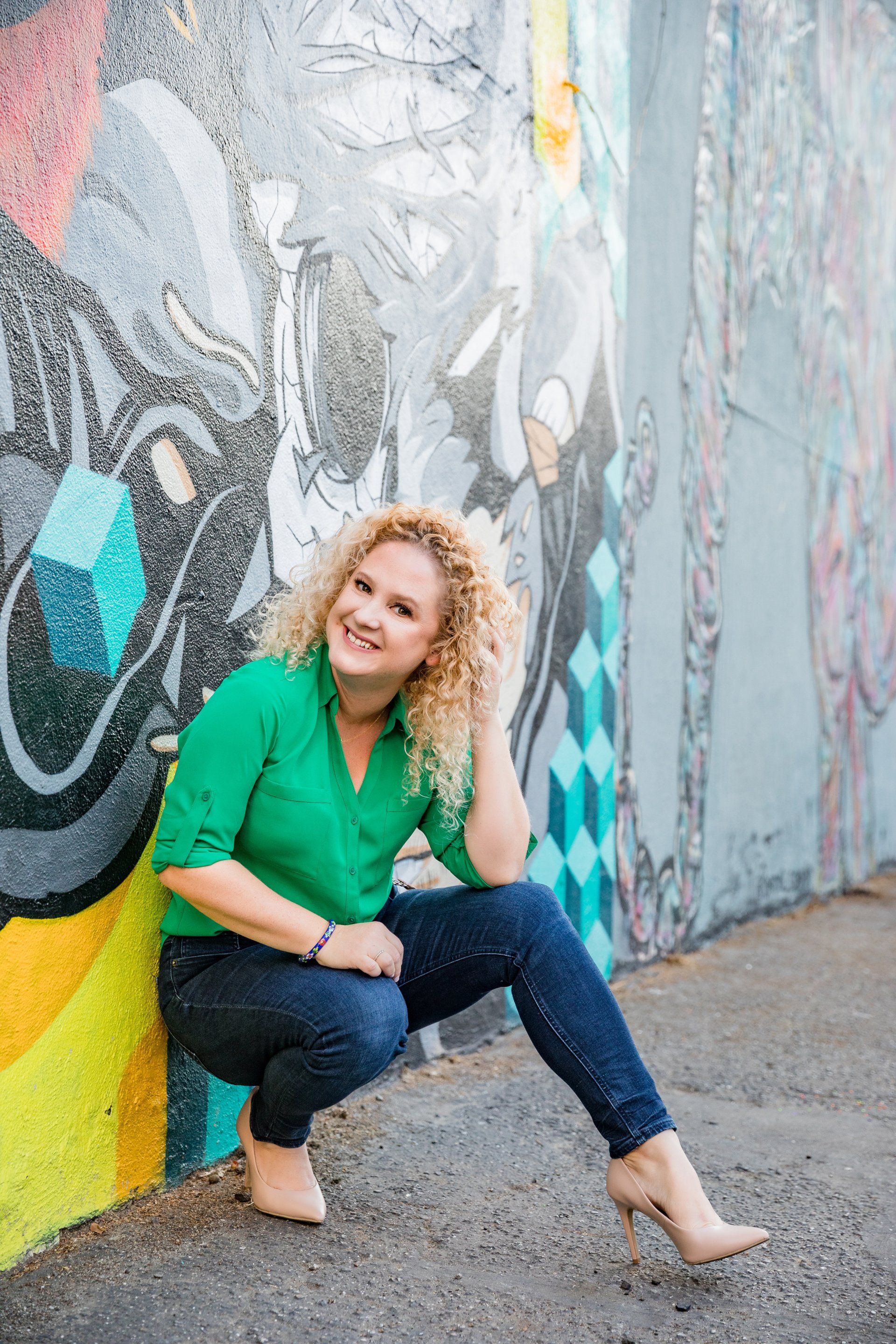 A woman is kneeling down in front of a graffiti wall.